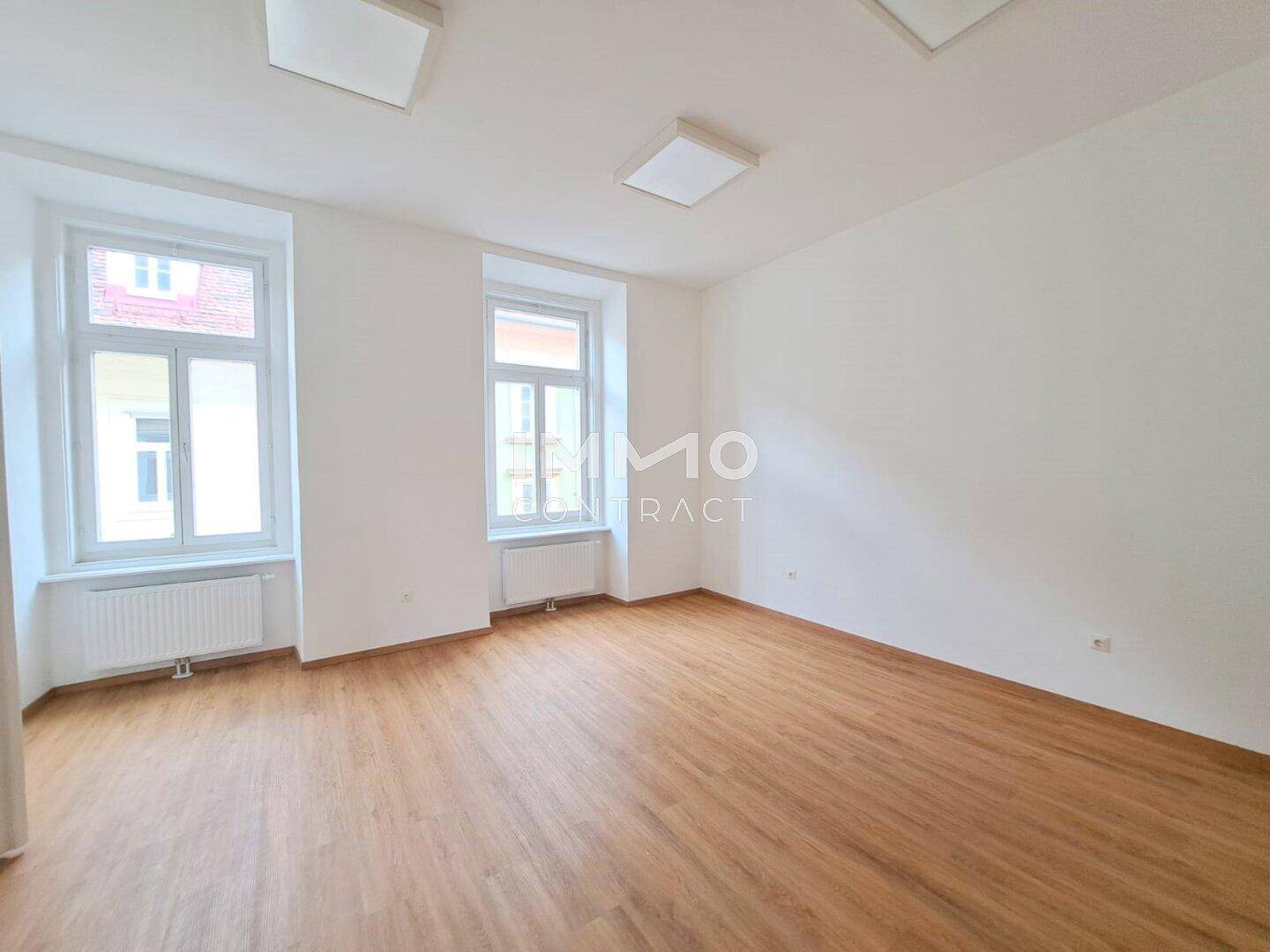 Heller, leerer Raum mit Holzboden und zwei großen Fenstern, bietet vielseitige Nutzungsmöglichkeiten.