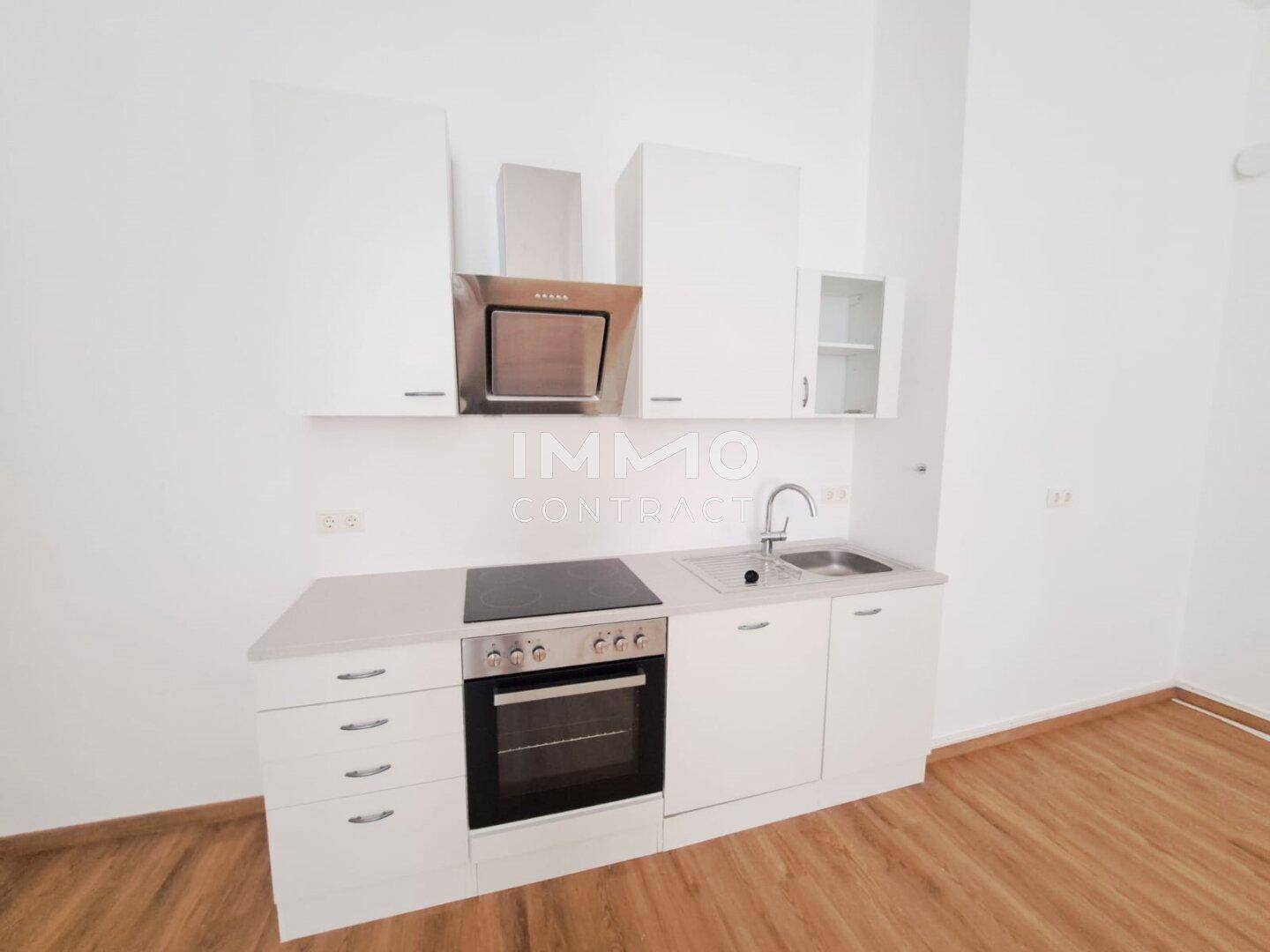 Kompakte, moderne Küchenzeile mit weißen Schränken, Kochfeld und Backofen, ideal für kleine Wohnungen.