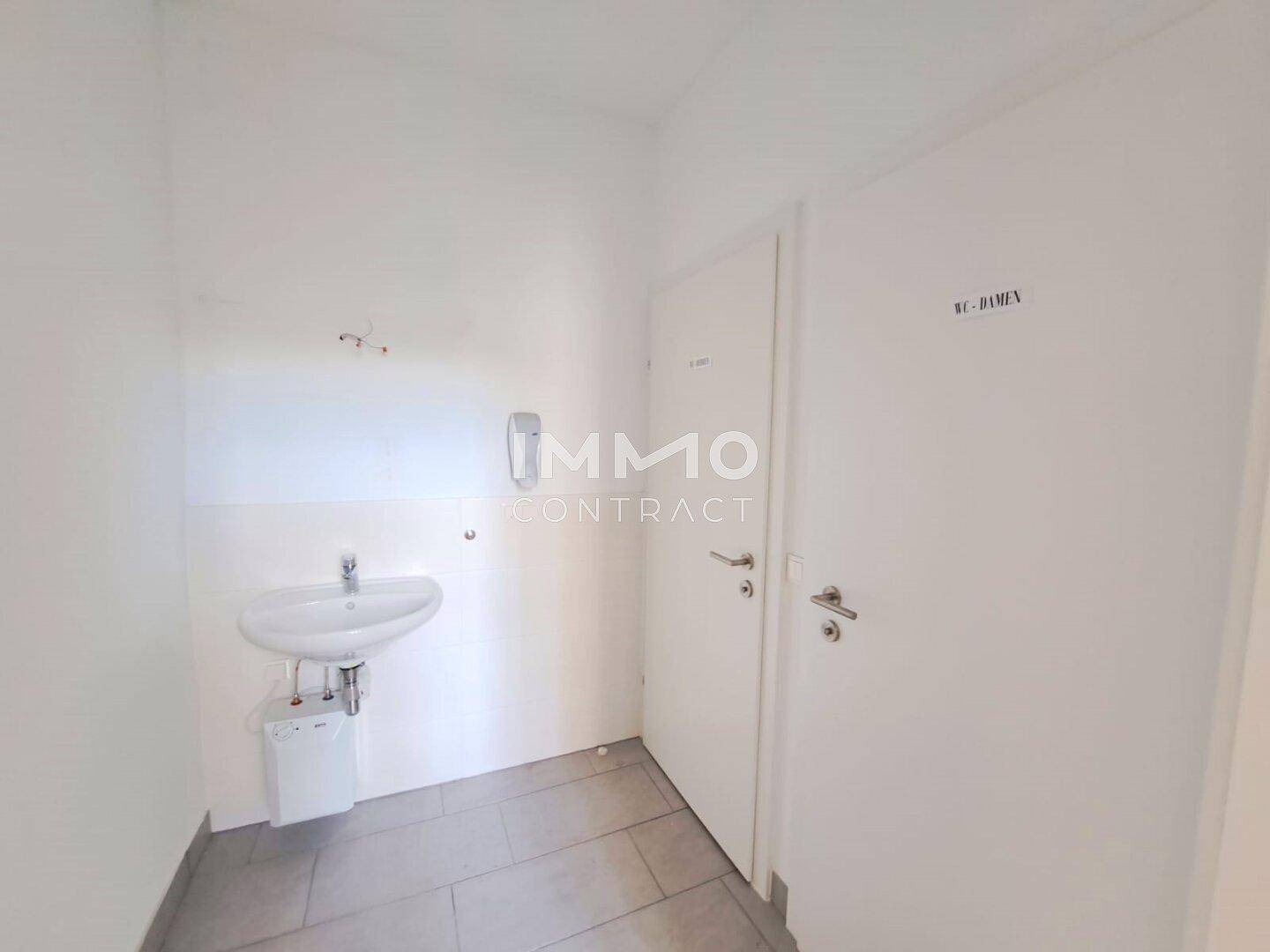 Einfacher Toilettenbereich mit Waschbecken und gefliestem Boden, mit separaten Zugängen.
