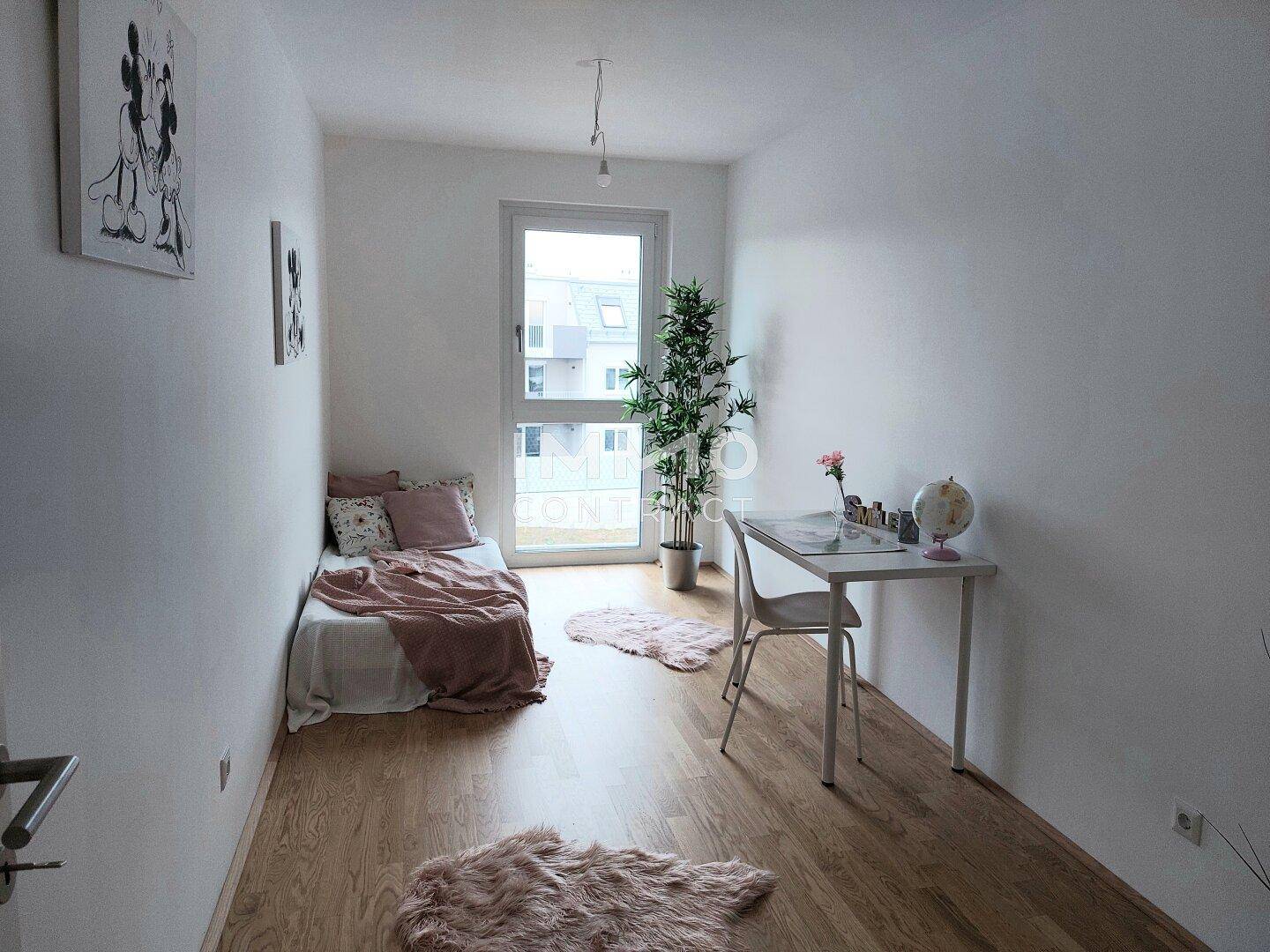 Gemütliches Schlafzimmer mit Holzboden, Schreibtisch und großem Fenster.