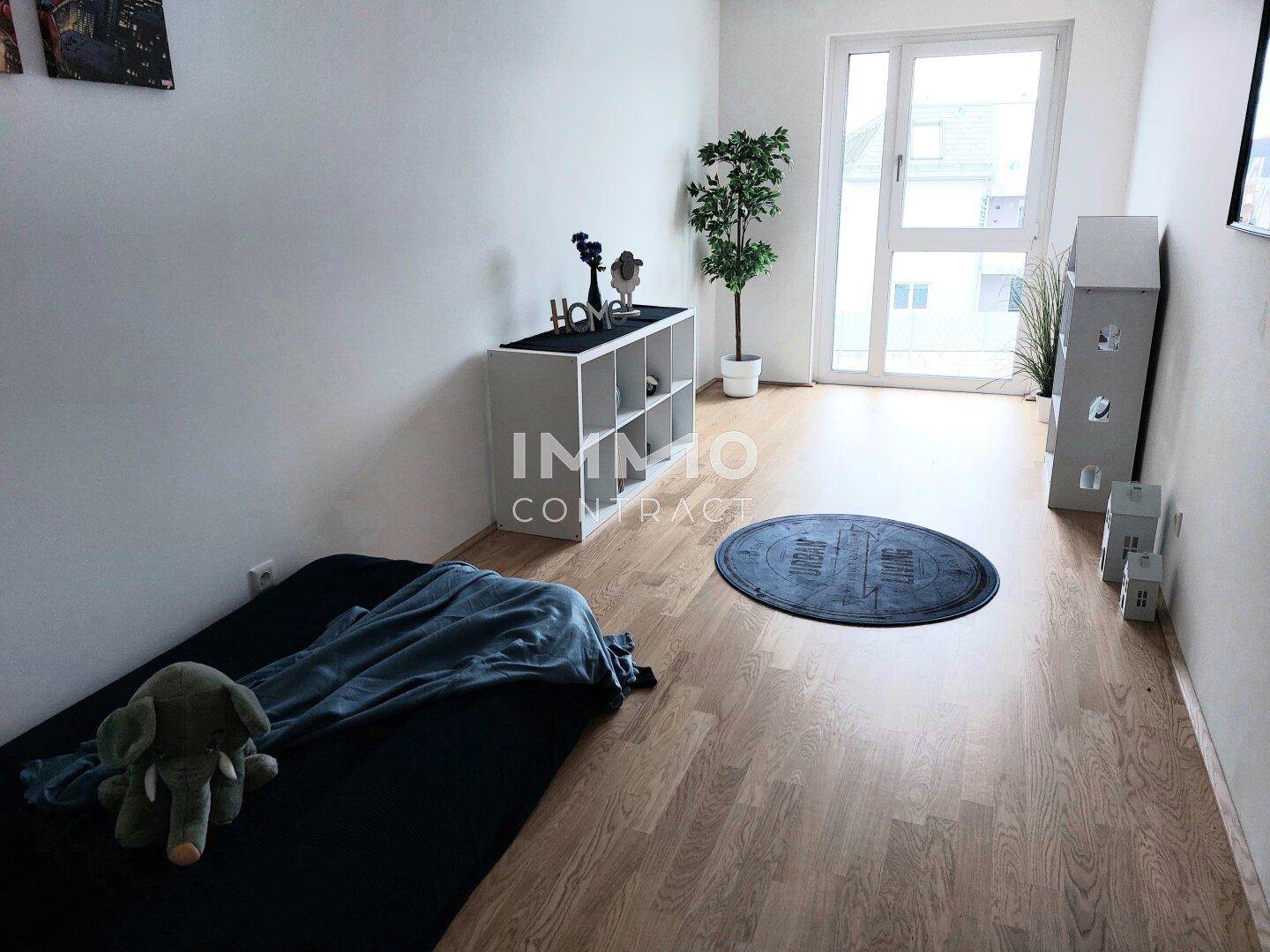 Helles Kinderzimmer mit Holzboden, großem Fenster und einfacher Einrichtung.