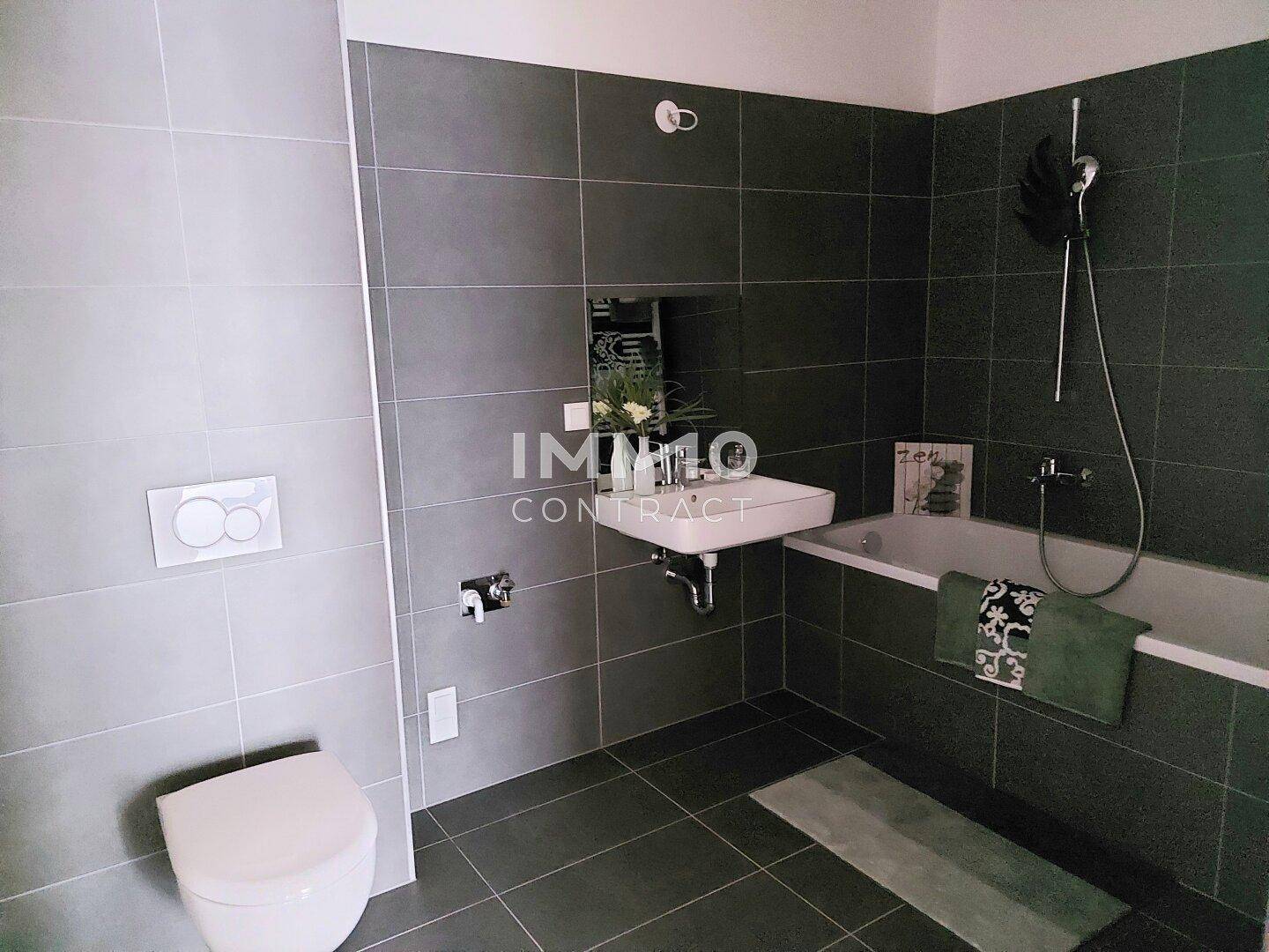 Modernes Badezimmer mit dunklen Fliesen, Badewanne und wandhängendem WC.