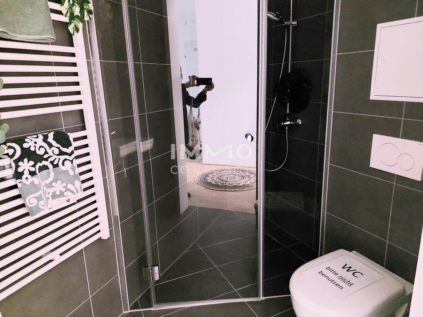 Modernes Gäste-WC mit Dusche, dunklen Fliesen und beheiztem Handtuchhalter.