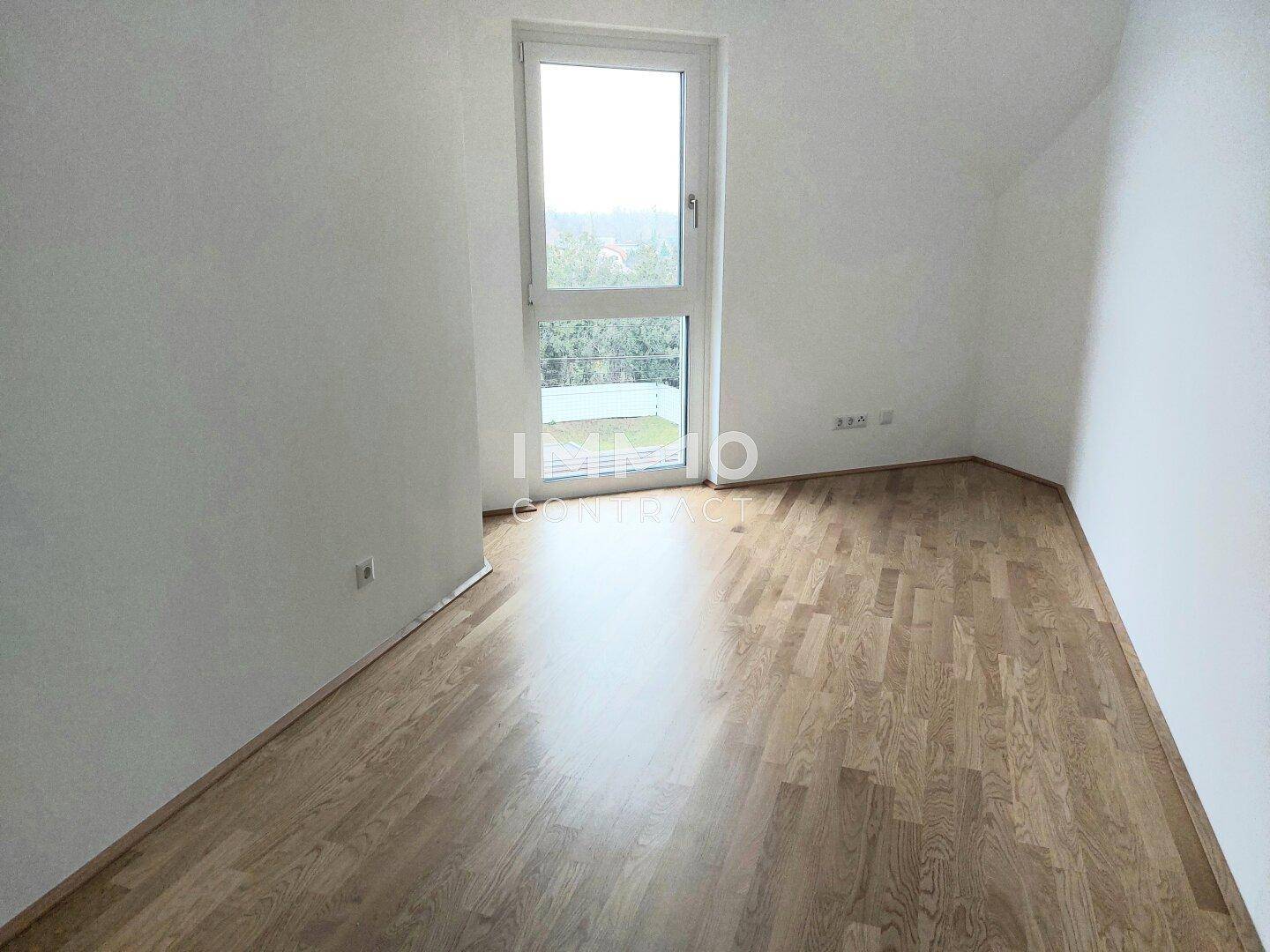 Helles Schlafzimmer mit Parkettboden und einem großen Fenster, das einen schönen Blick ins Grüne bietet.