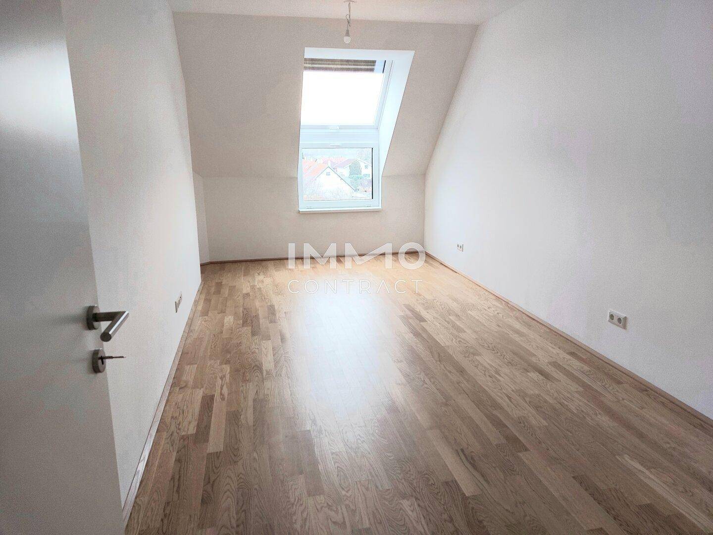 Gemütliches Schlafzimmer im Dachgeschoss mit Parkettboden, schrägen Wänden und einem Dachfenster.
