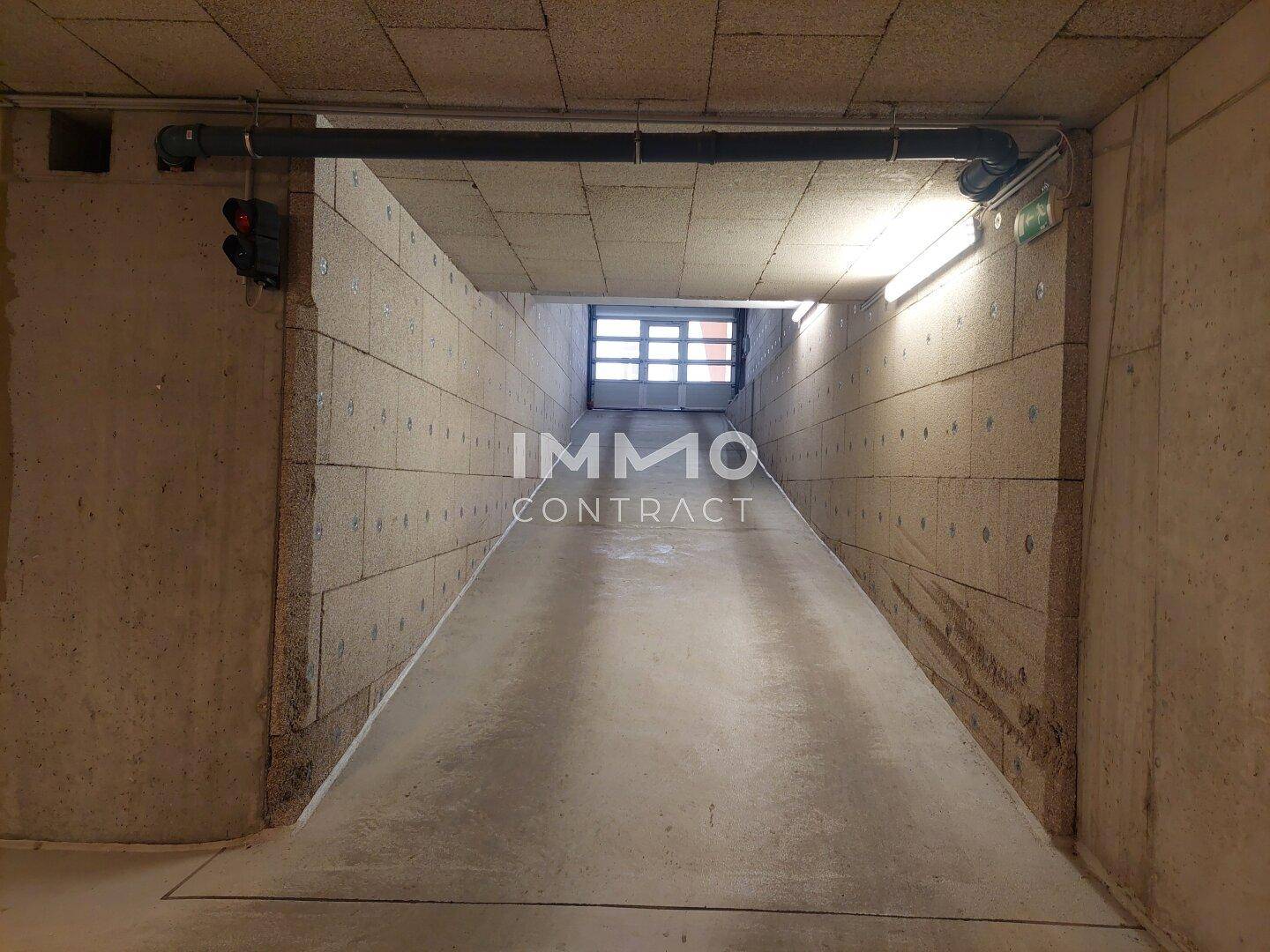 Rampe führt hinunter in die Tiefgarage mit Betonwänden und Beleuchtung.