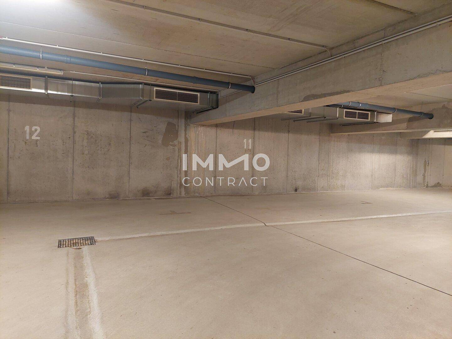 Geräumiger Stellplatz in der Tiefgarage mit sichtbaren Lüftungsrohren und Betonoberflächen.