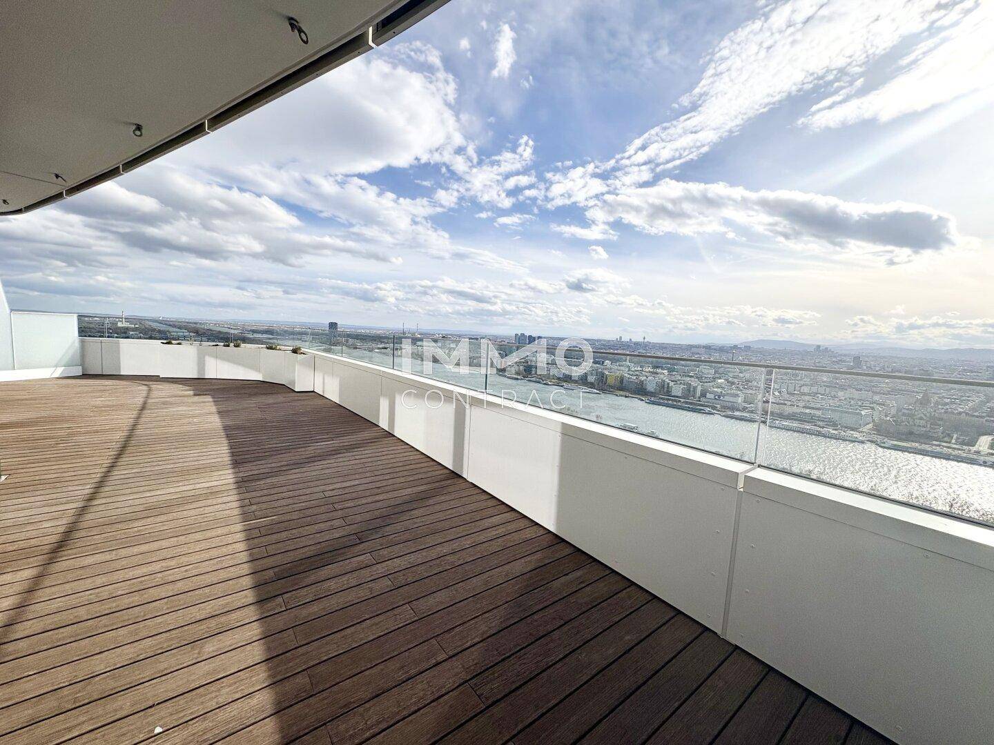 Großzügige Terrasse mit Holzdielen und Glasgeländer, ideal für Entspannung mit weitem Stadtblick.