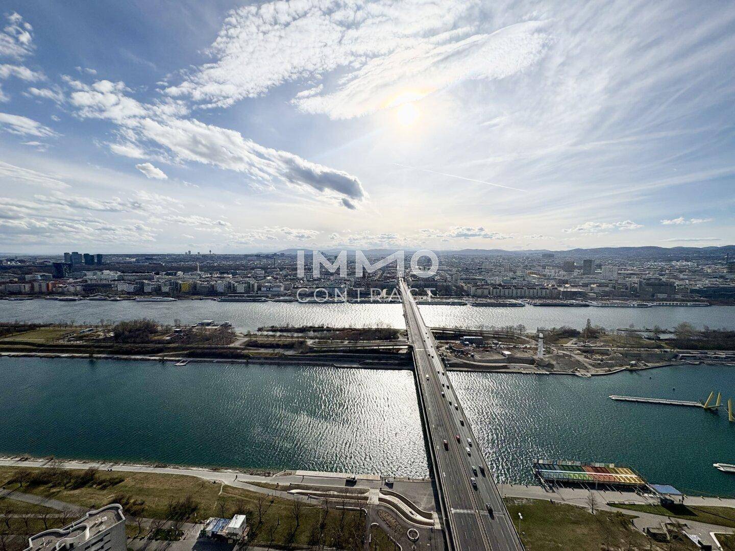 Panoramablick über die Stadt mit Fluss, Brücke und umliegender Bebauung unter blauem Himmel.