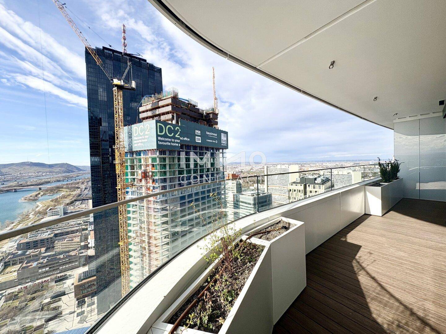Terrasse mit Blick auf ein modernes Hochhaus im Bau und die umliegende Stadtlandschaft.