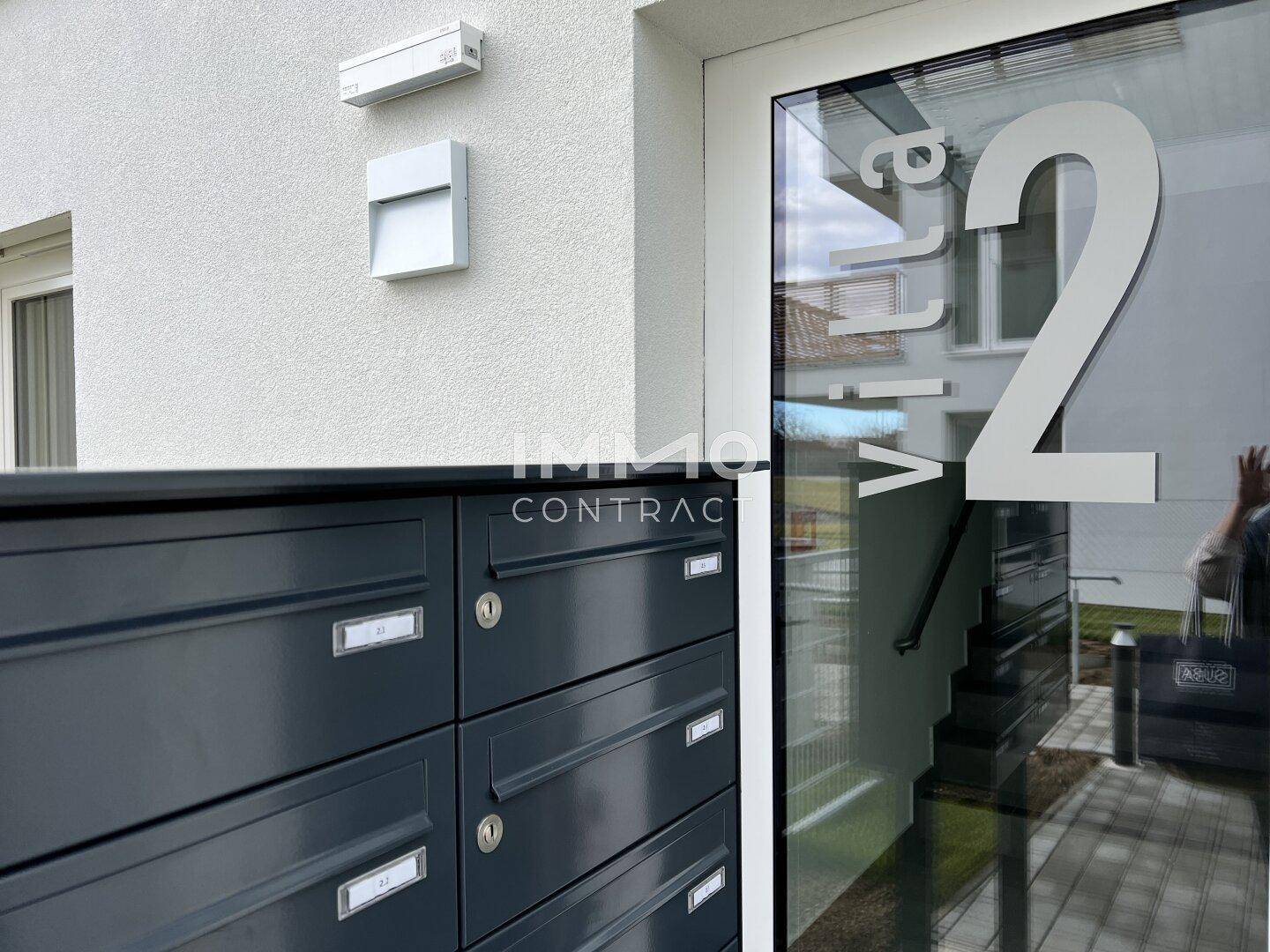 Eingangsbereich einer modernen Villa mit Briefkästen und einer großen Glasfassade.