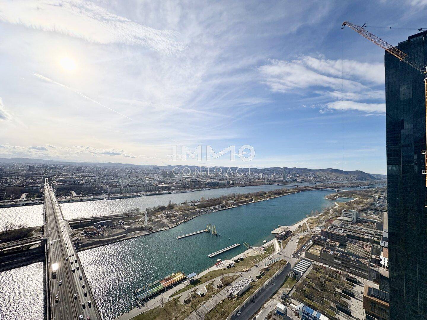 Weitläufiger Blick über die Stadt mit Fluss, Brücke und modernen Gebäuden unter sonnigem Himmel.