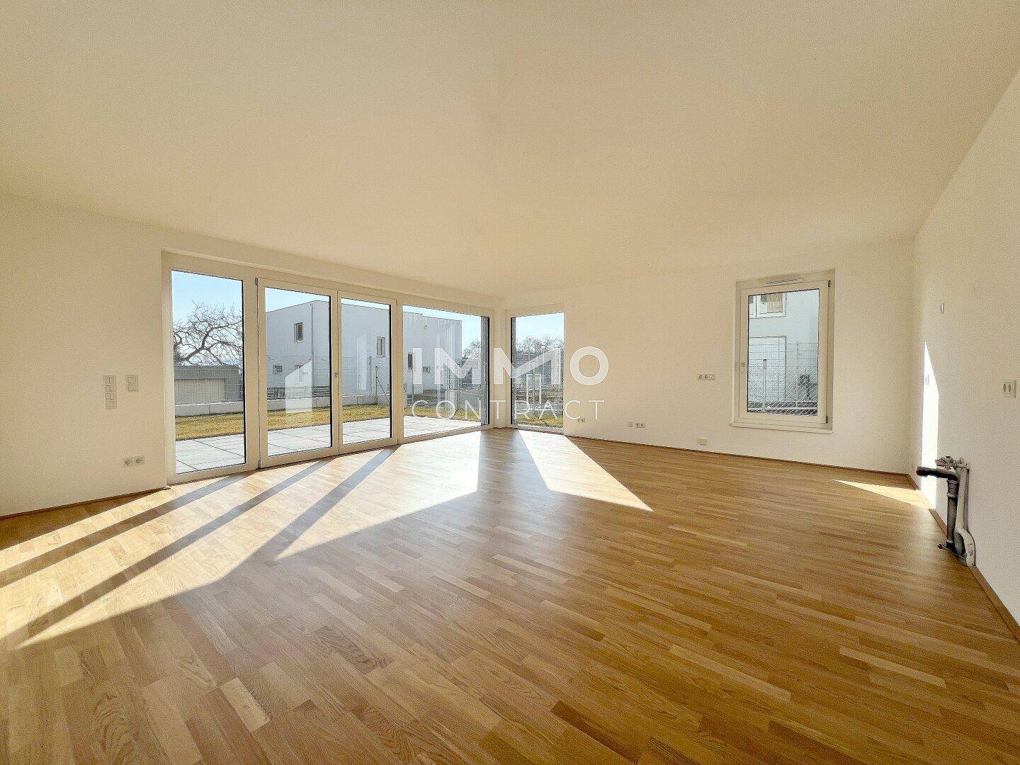 Geräumiger Wohnbereich mit viel Tageslicht, hellem Parkett und Blick ins Grüne.