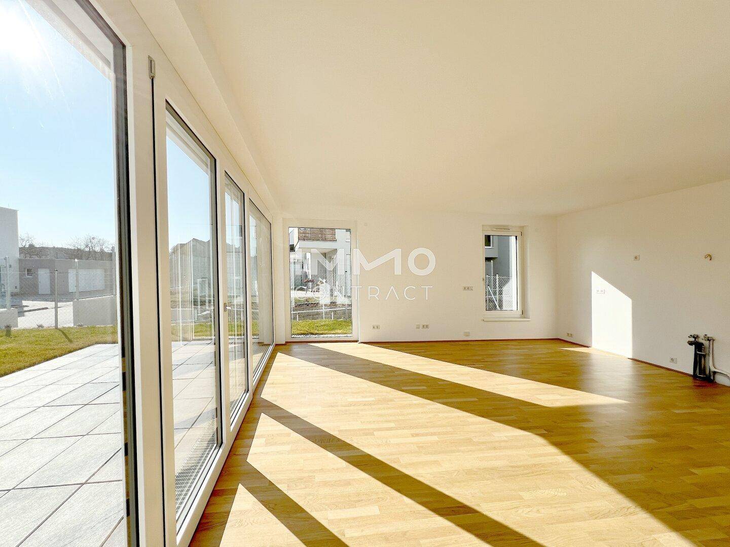 Sonniges Wohnzimmer mit großen Glasfronten, Parkettboden und direktem Zugang zum Außenbereich.