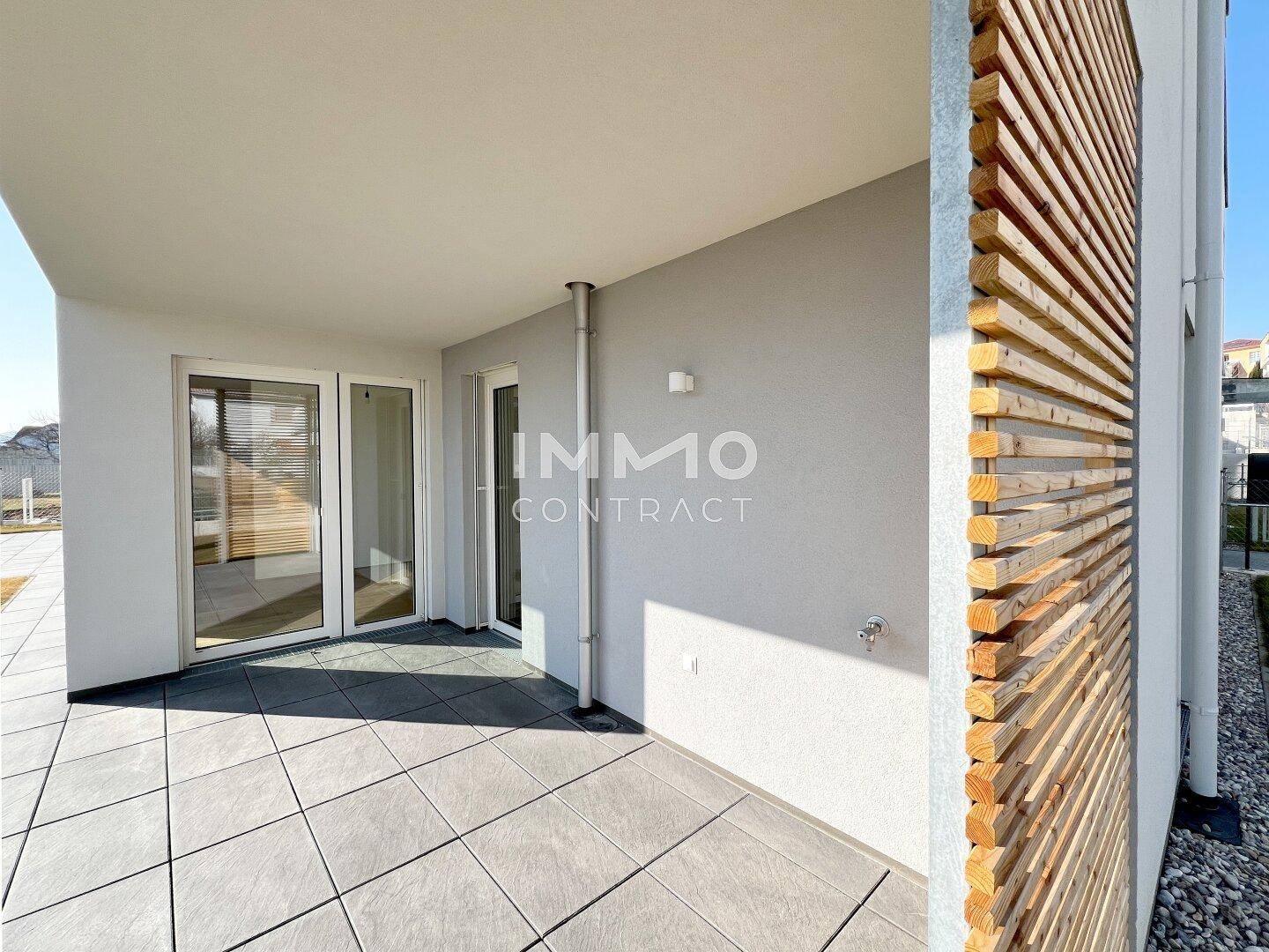 Überdachte Terrasse mit modernen Fliesen und dekorativen Holzelementen an der Fassade.