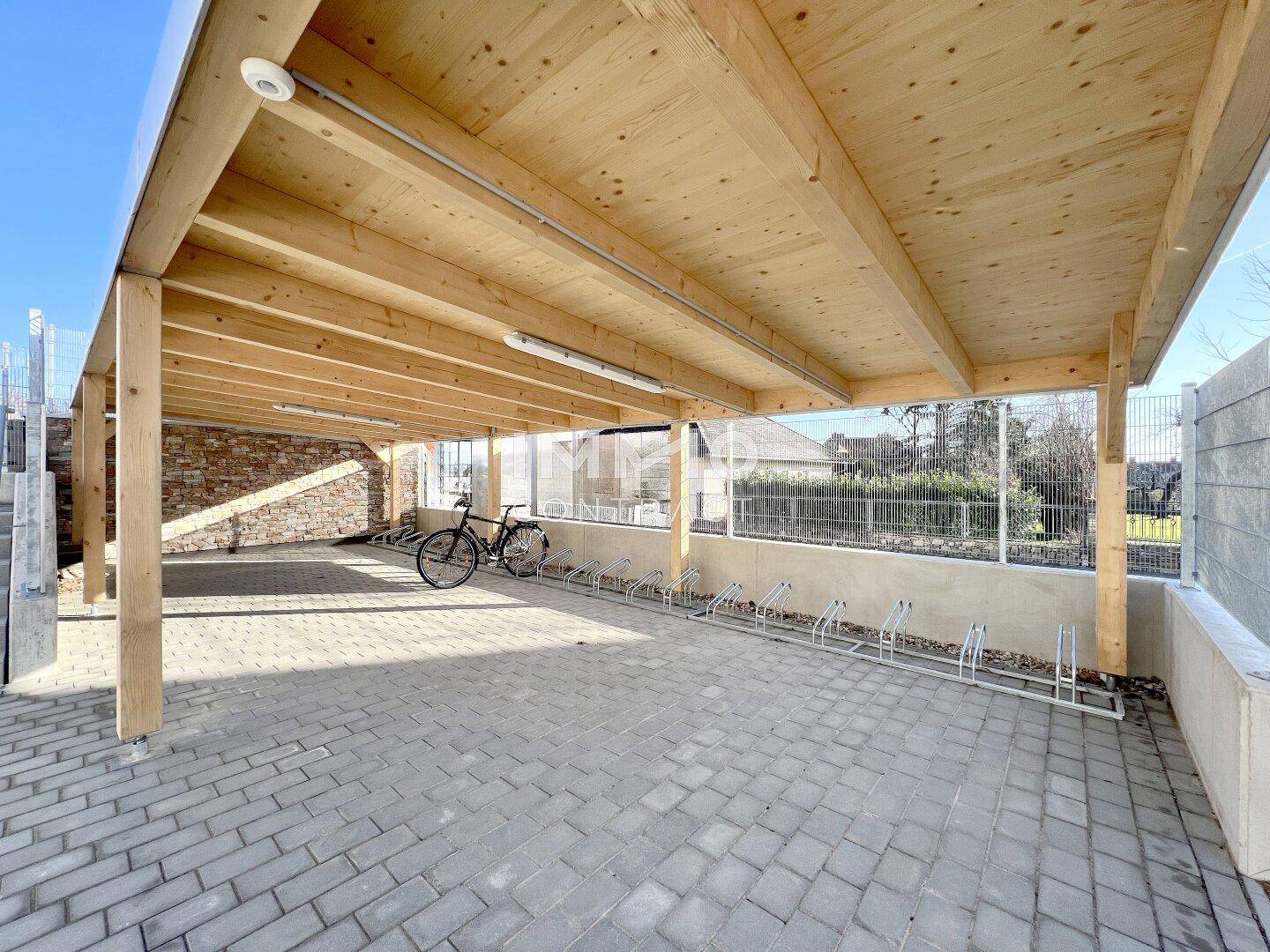 Überdachter Fahrradabstellplatz und Carport mit robuster Holzkonstruktion und Pflastersteinen.
