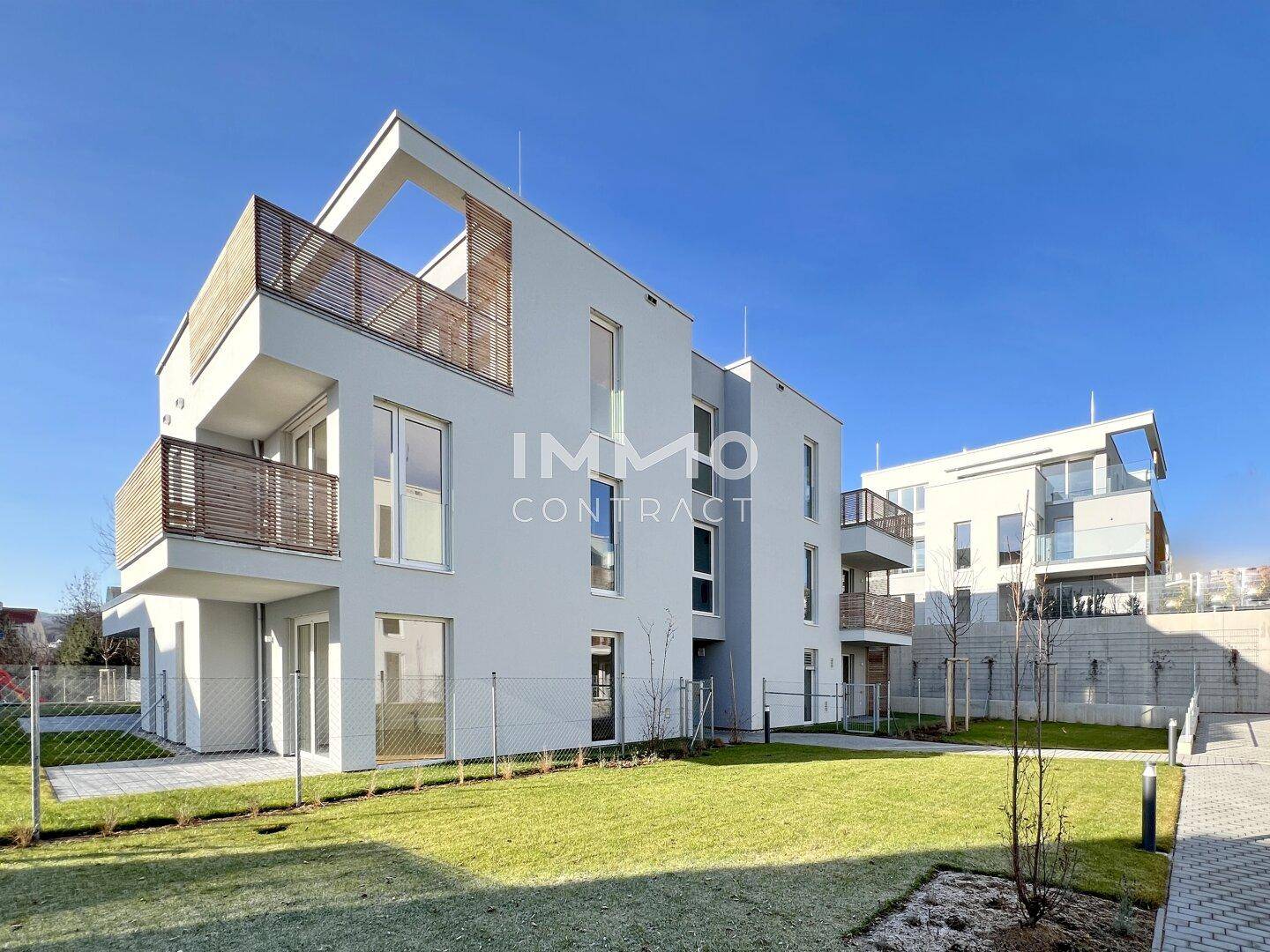 Moderne Wohnanlage mit mehreren Gebäuden, Balkonen und gepflegten Rasenflächen unter blauem Himmel.