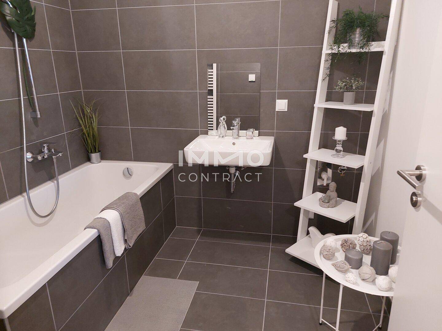 Modernes Badezimmer mit Badewanne, Waschbecken, beheiztem Handtuchhalter und grauen Fliesen.