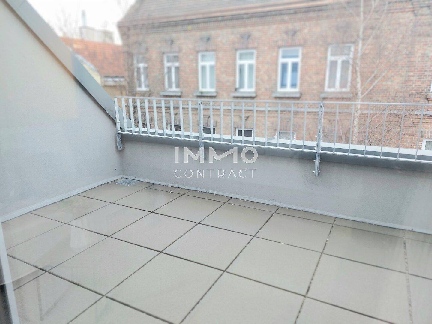 Geräumige Terrasse mit Fliesenboden und Blick auf ein gegenüberliegendes Gebäude.