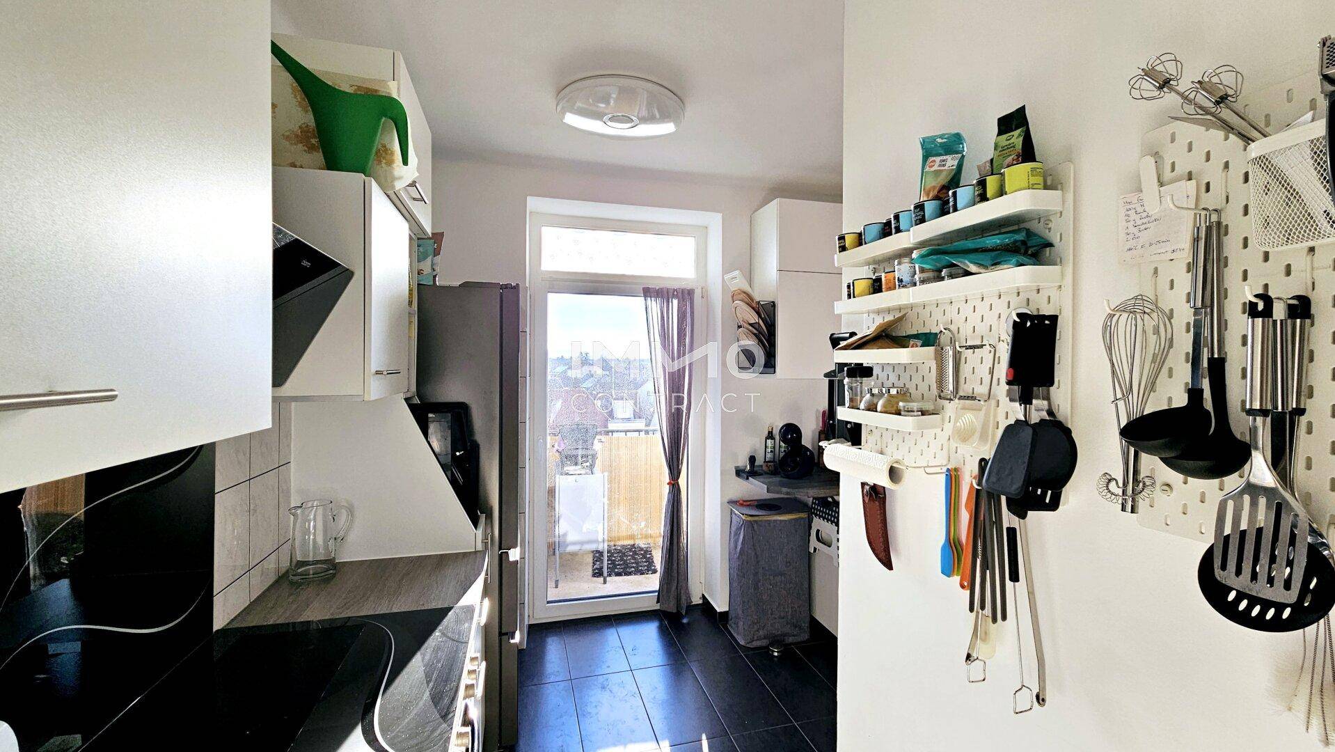 Kleine Küche mit weißen Schränken, dunklem Fliesenboden und direktem Balkonzugang.