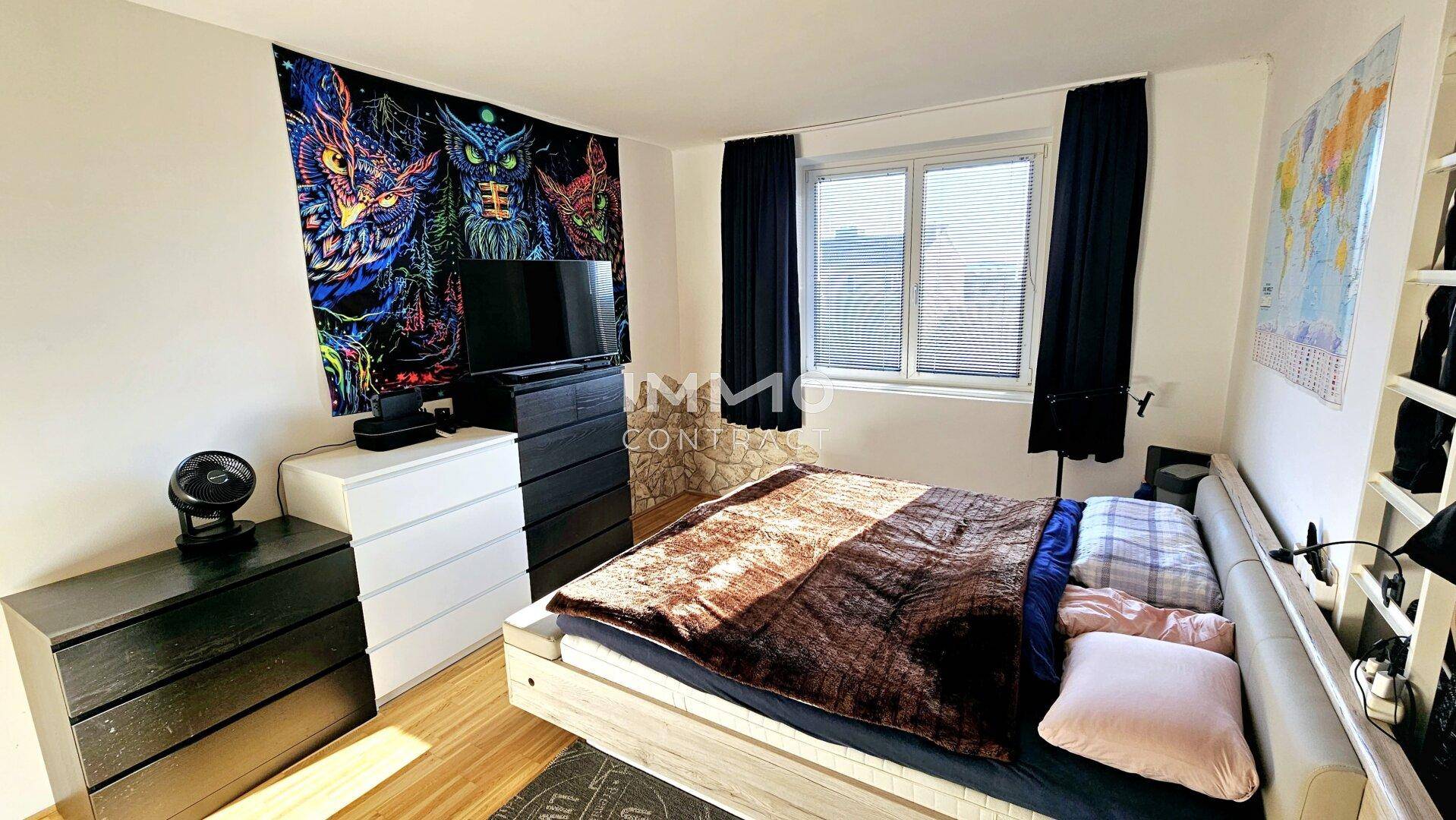 Schlafzimmer mit Holzboden, großem Bett und farbenfroher Wanddekoration.