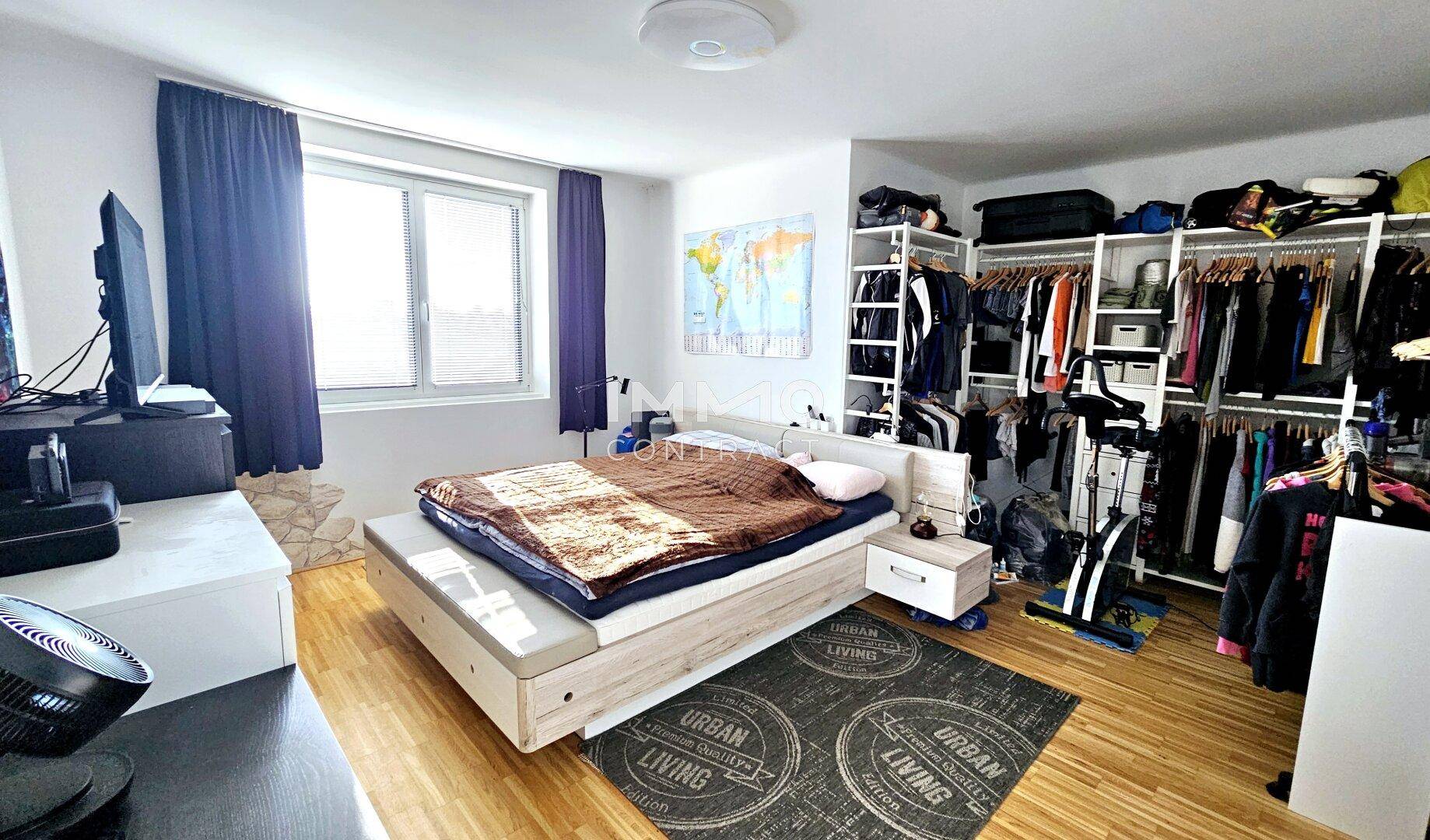 Schlafzimmer mit Holzboden, großem Bett und offenem begehbarem Kleiderschrankbereich.