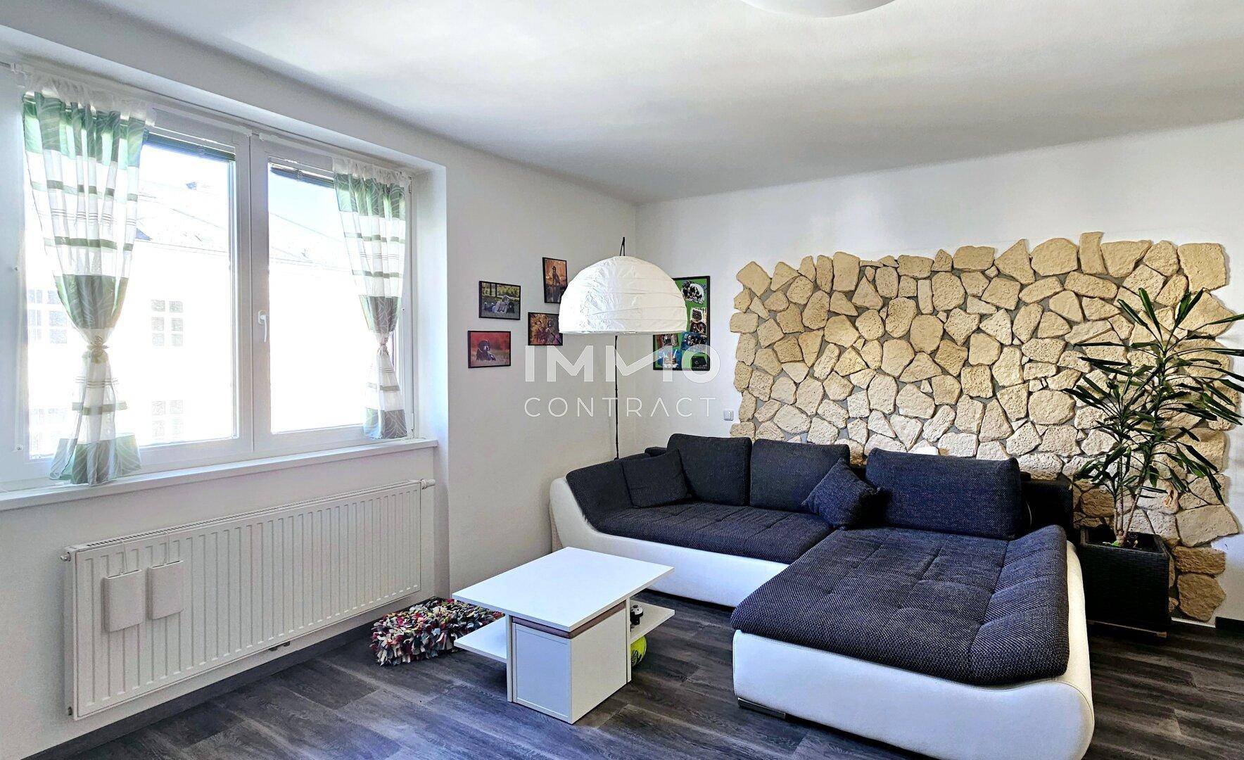 Helles Wohnzimmer mit bequemer Sitzecke, Laminatboden und einer markanten Steinwand.