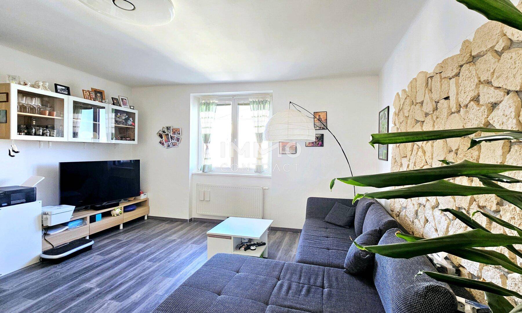 Gemütliches Wohnzimmer mit L-förmigem Sofa, Laminatboden und einer dekorativen Steinwand.