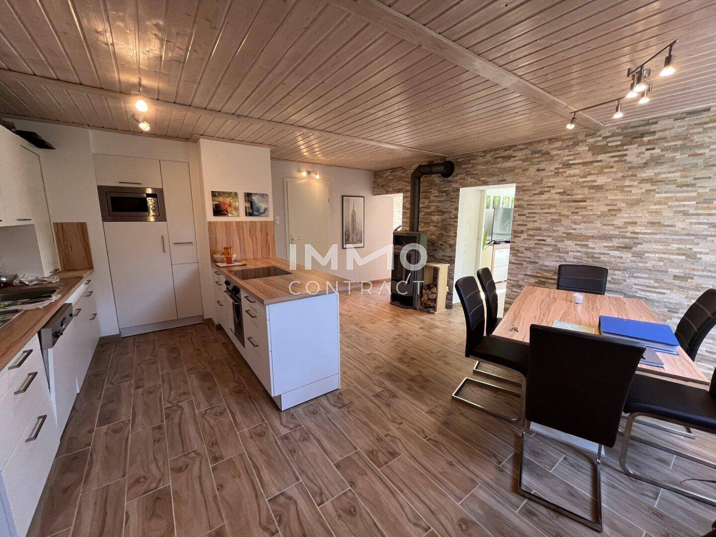 Offene Wohnküche mit Essbereich, Holzdecke und Kaminofen als Blickfang.