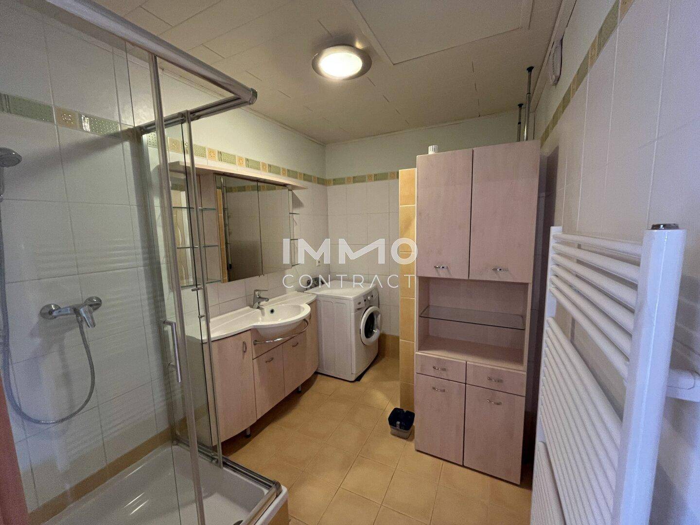 Funktionales Badezimmer mit Dusche, Waschbecken, WC und Waschmaschine.