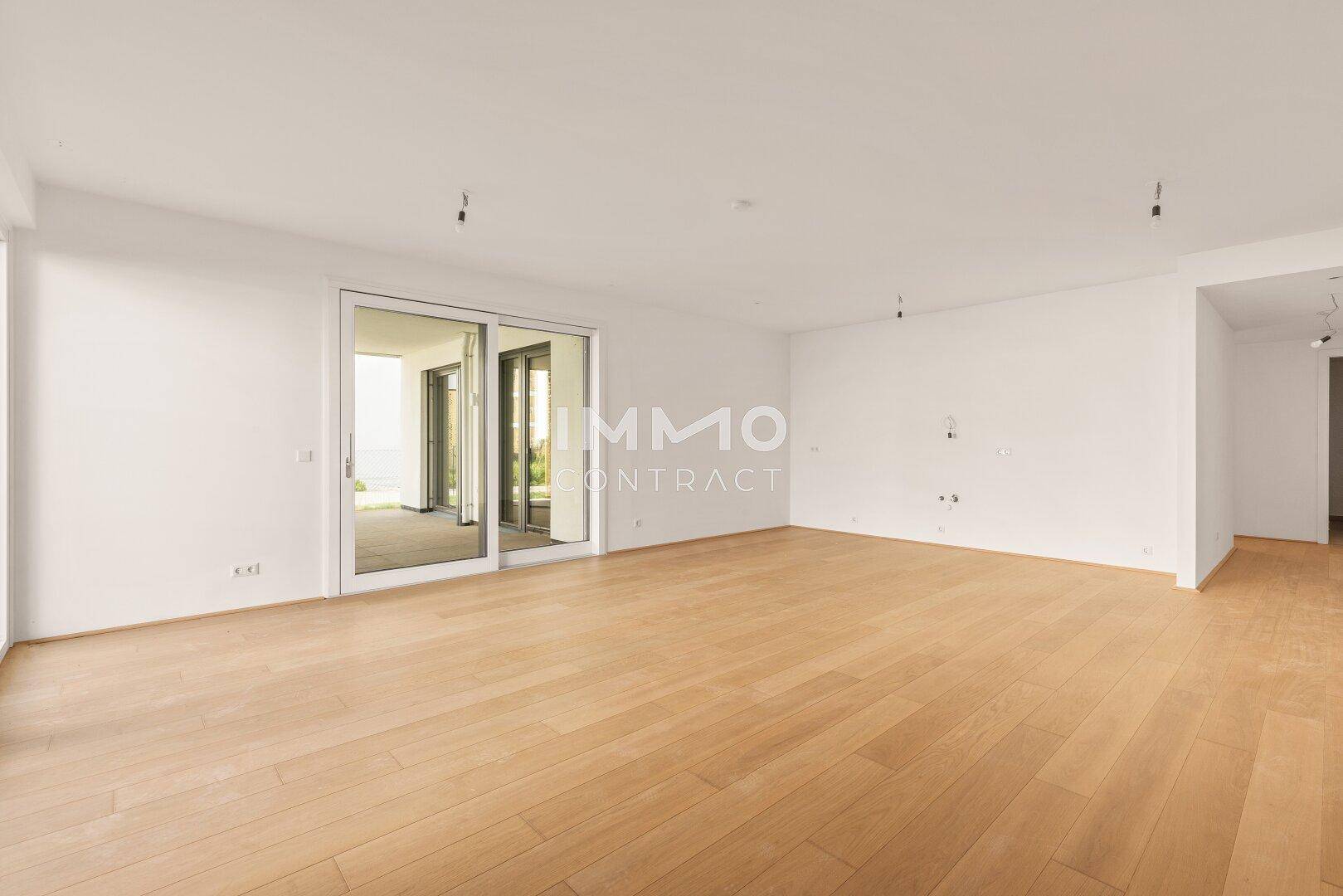 Geräumiges, unmöbliertes Wohnzimmer mit hellem Holzboden und Zugang zu einer Außenterrasse.