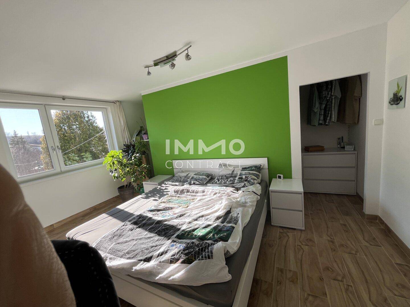 Helles Schlafzimmer mit grüner Akzentwand, Holzoptik-Fliesenboden und Einbauschrank.