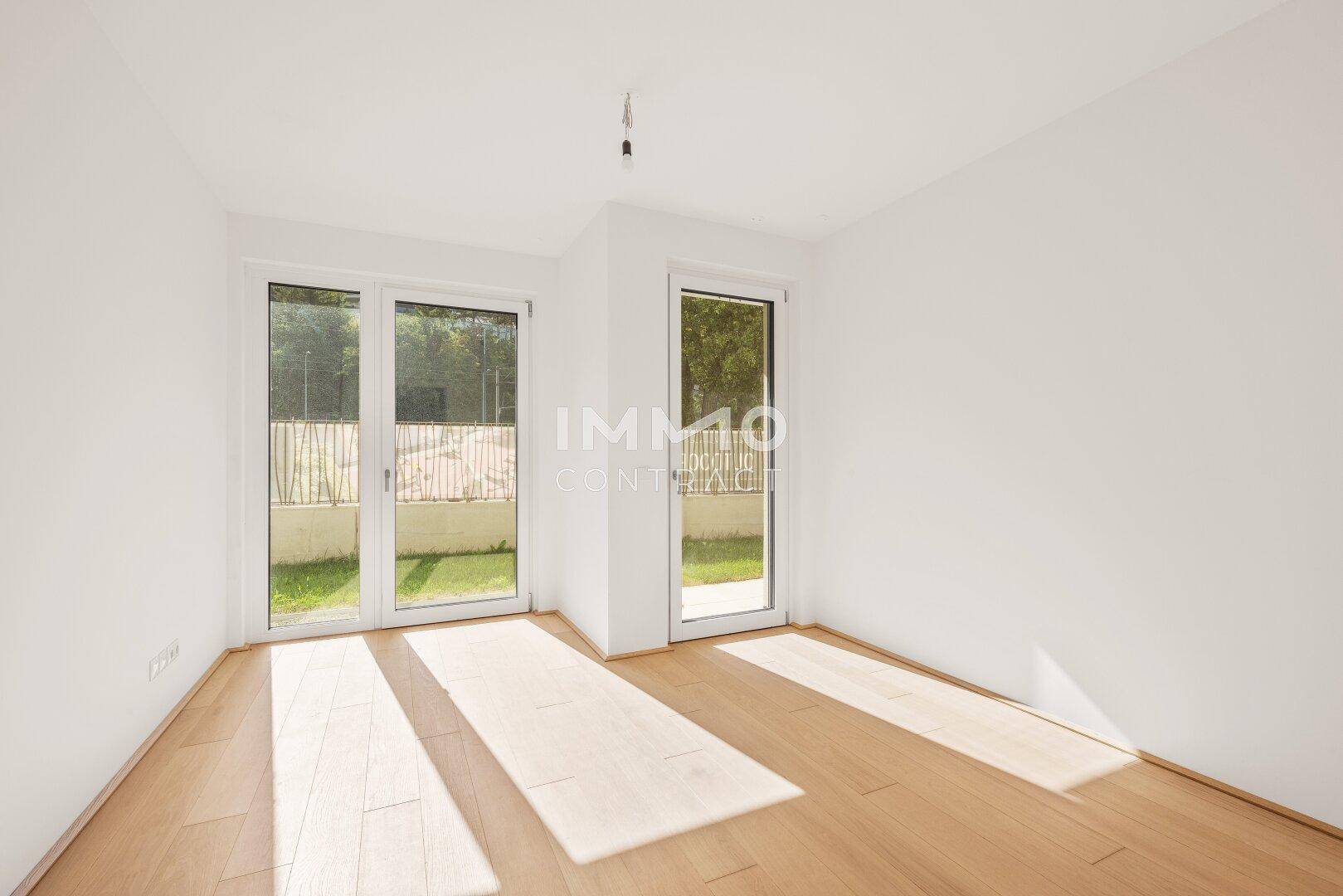 Helles Schlafzimmer mit Holzboden und zwei Glastüren, die direkten Zugang zum Außenbereich ermöglichen.