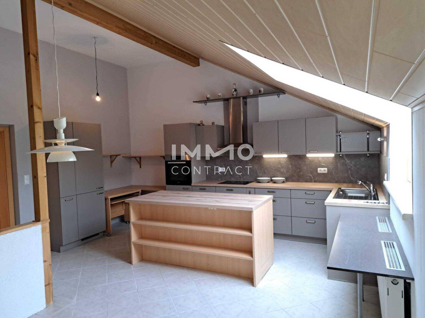Geräumige Küche im Dachgeschoss mit Kücheninsel, Dachschräge und modernen grauen Schränken.
