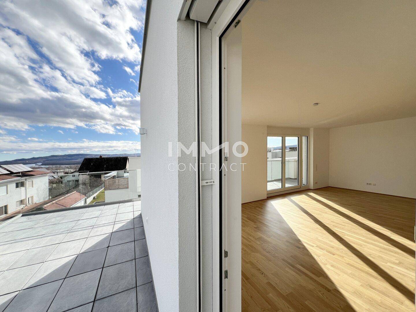 Heller, leerer Wohnbereich mit Holzboden, großen Fenstern und Zugang zur Terrasse mit Weitblick.