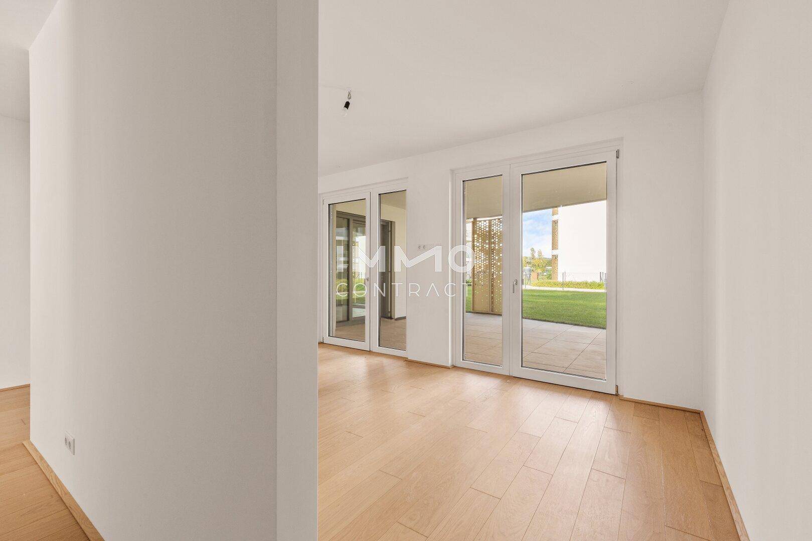 Geräumiger, heller Raum mit Holzboden und mehreren Glastüren, die zu einem Außenbereich führen.