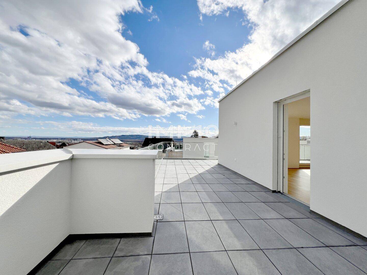 Weitläufige Dachterrasse mit modernen Fliesen, weißer Fassade und Panoramablick in die Ferne.