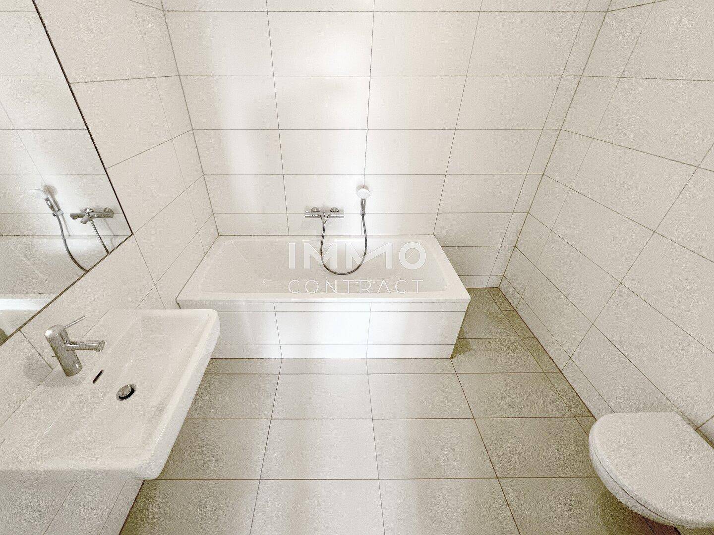 Helles Badezimmer mit Badewanne, WC und großformatigen weißen Fliesen.
