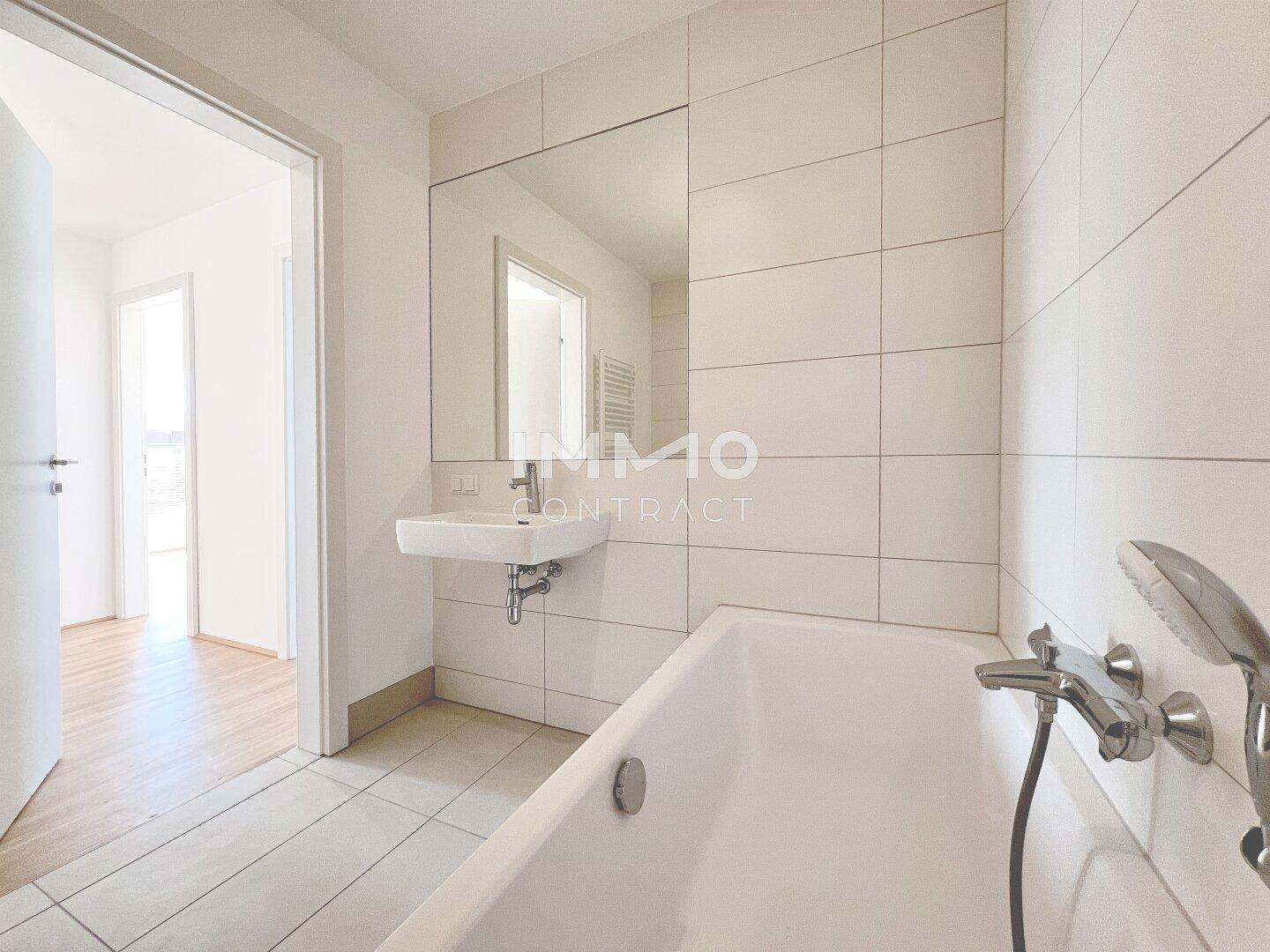 Geräumiges Badezimmer mit Badewanne, großem Spiegel und Zugang zu einem weiteren Raum.