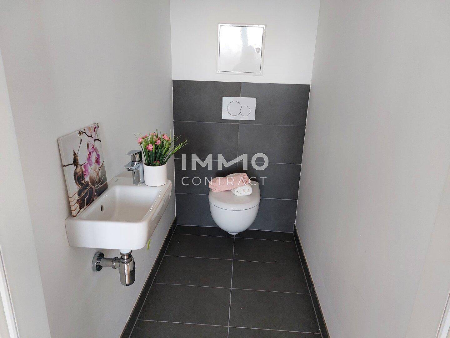 Modernes Gäste-WC mit dunklen Fliesen, wandhängendem WC und kleinem Waschbecken.