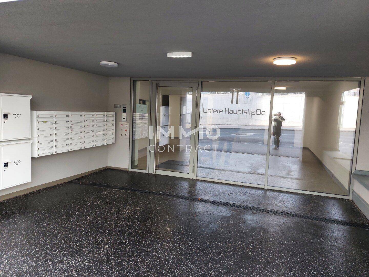 Eingangsbereich eines modernen Wohngebäudes mit Briefkästen und großer Glasfassade.