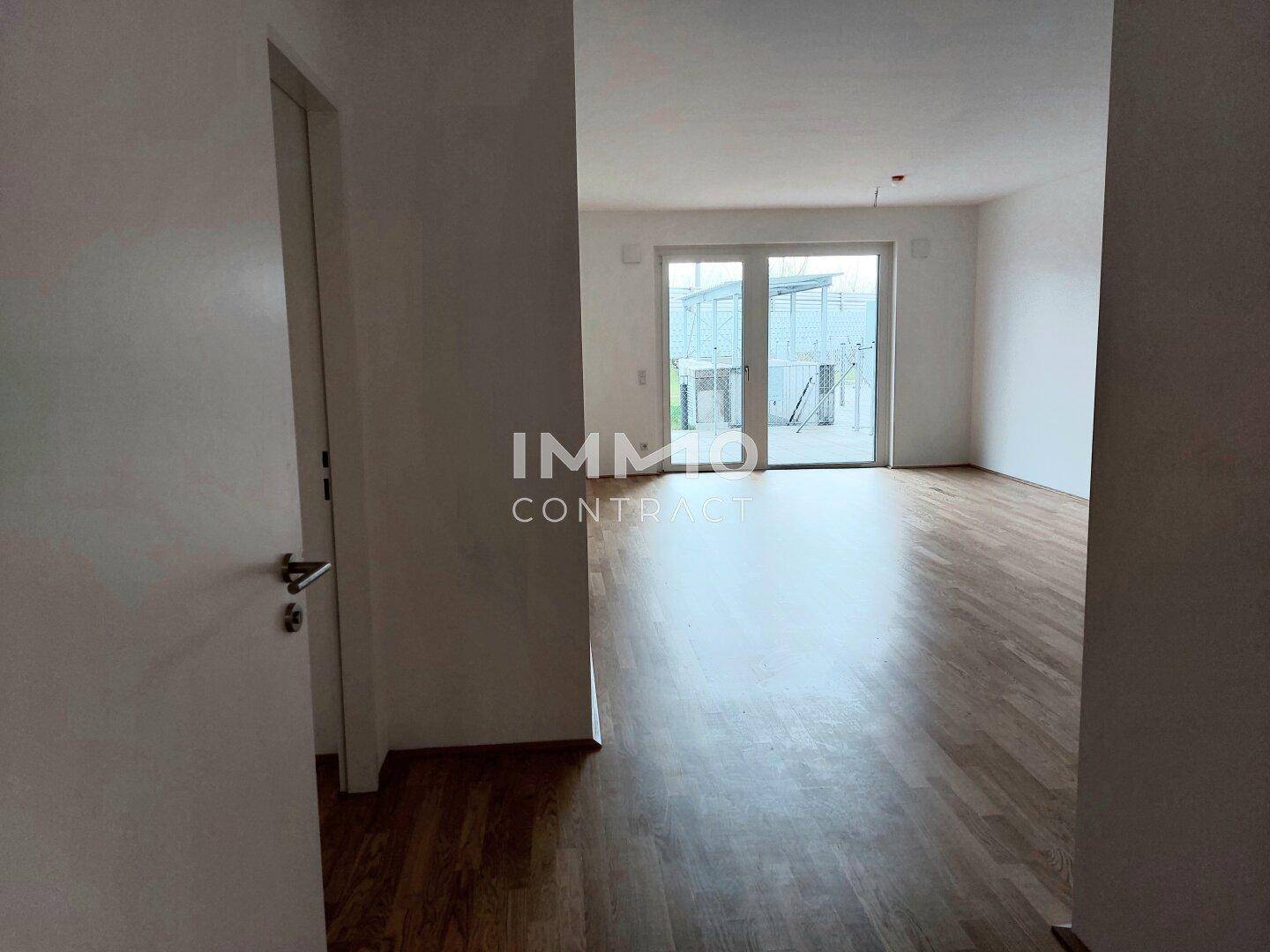 Großer, heller Wohnbereich mit Parkettboden und Zugang zum Außenbereich durch eine Fenstertür.