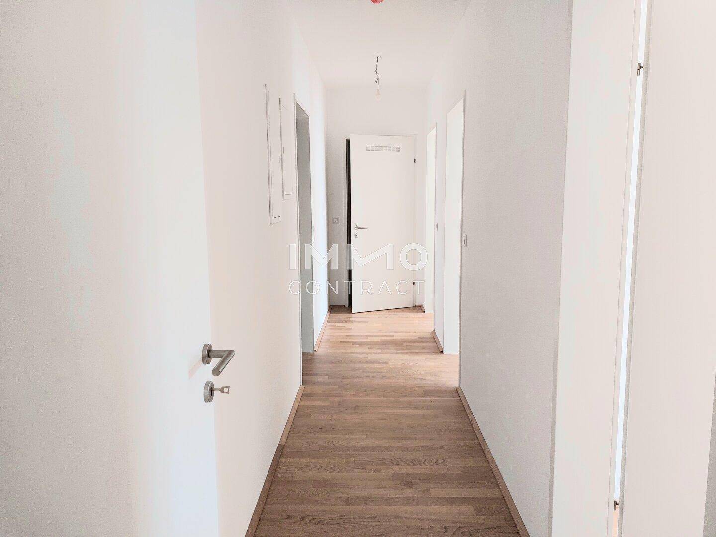 Heller Flur mit Holzboden und weißen Wänden, der zu den verschiedenen Zimmern führt.