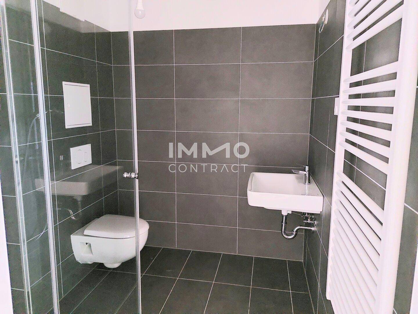Modernes Duschbad mit wandhängendem WC, Waschbecken und beheiztem Handtuchhalter.