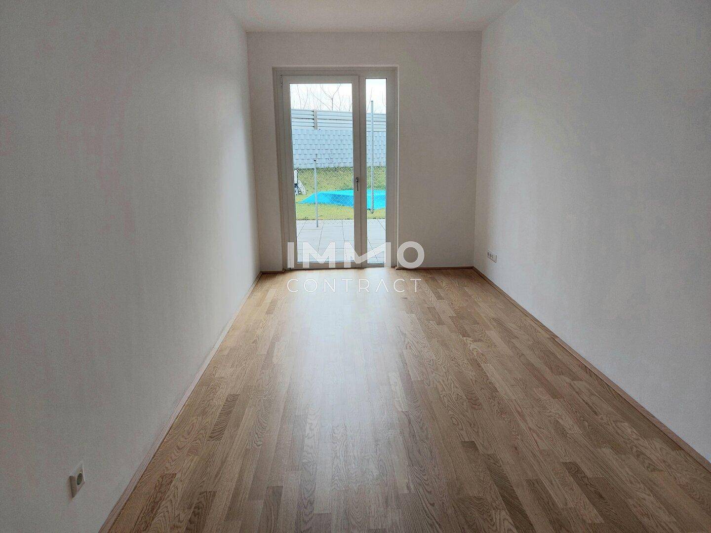 Helles Zimmer mit Parkettboden und großer Fenstertür, die viel Tageslicht hereinlässt.