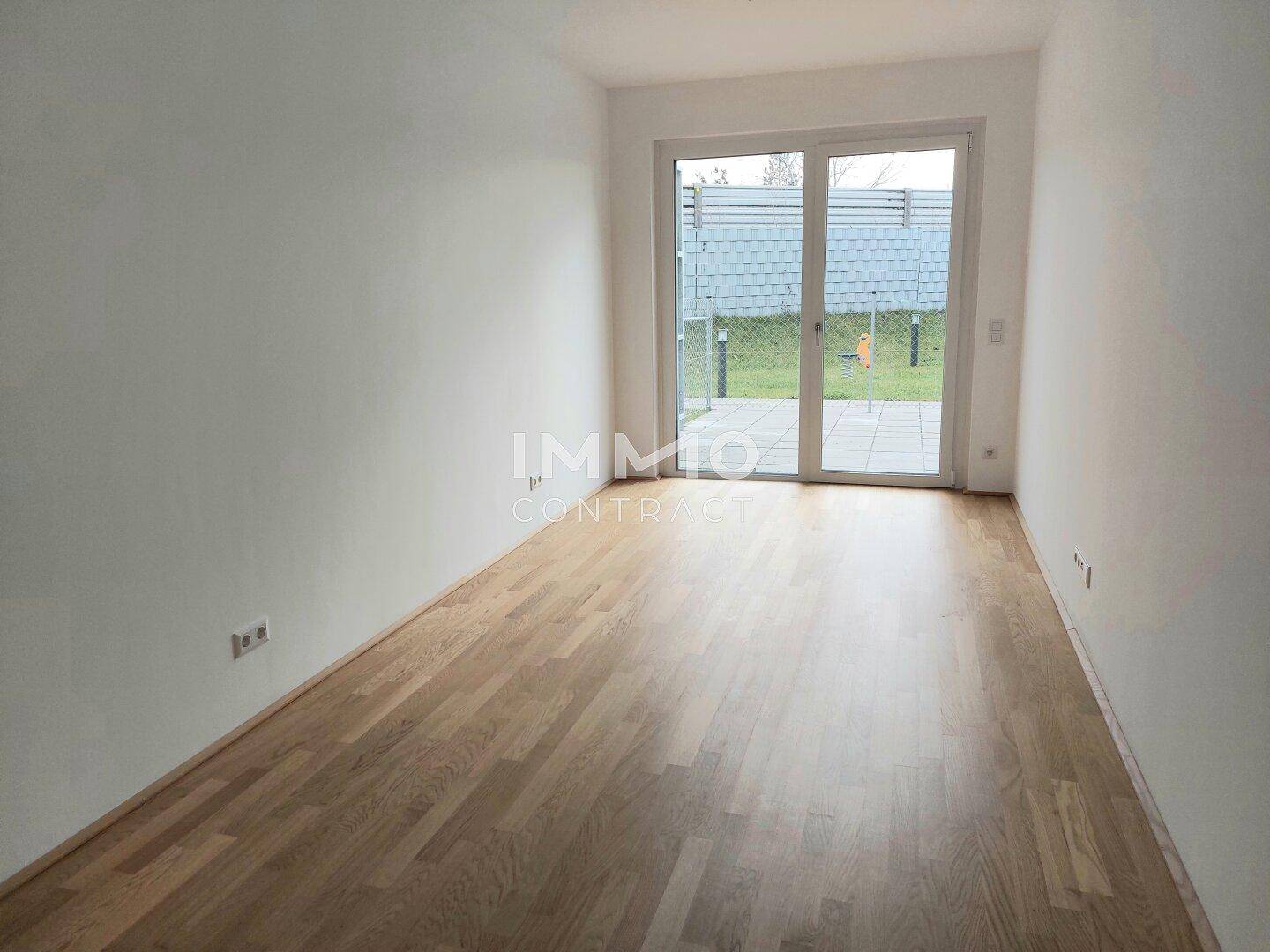 Lichtdurchflutetes Zimmer mit Holzboden und Blick ins Grüne durch die Fenstertür.
