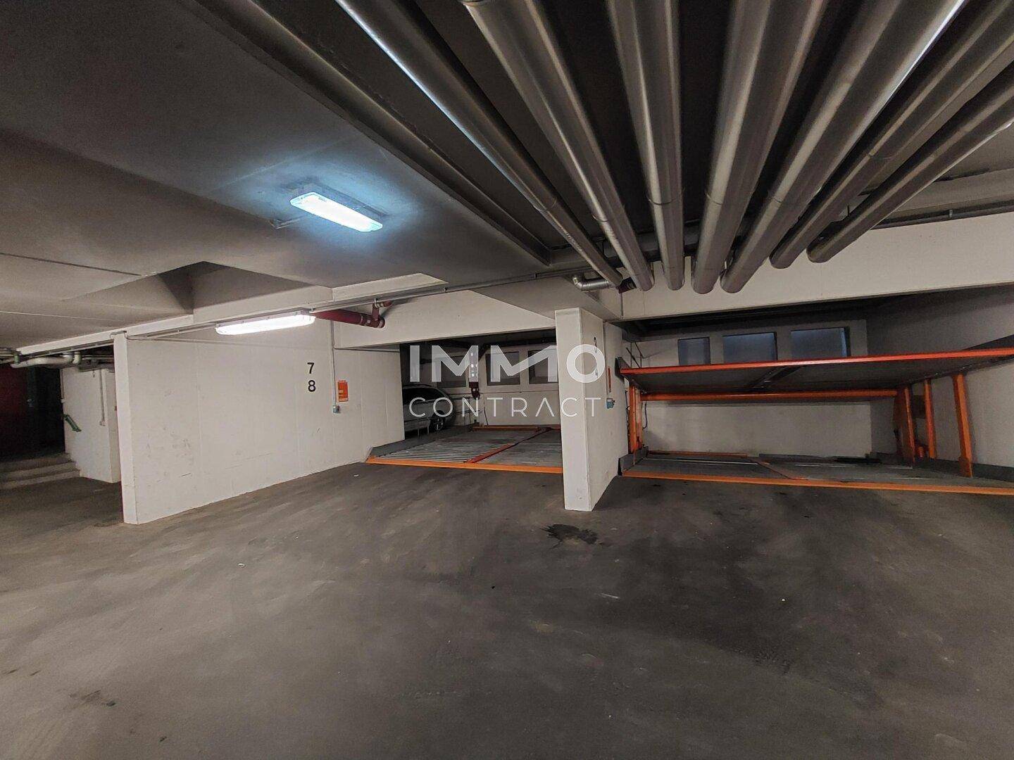 Helle Tiefgarage mit Autohebebühnen und sichtbaren Installationen an der Decke.