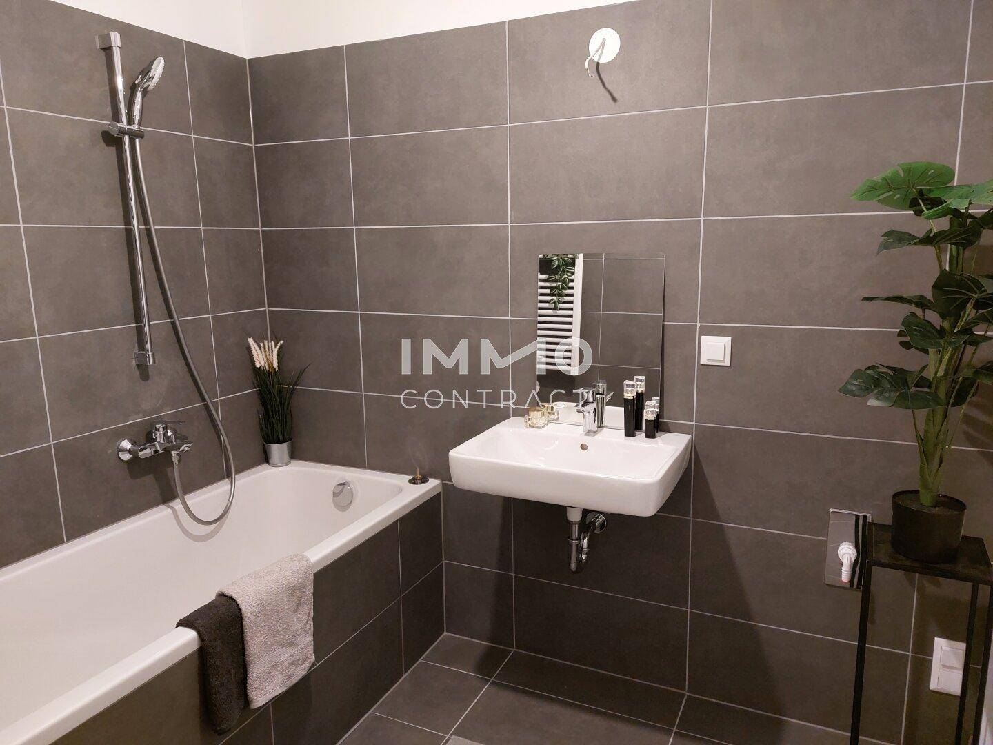 Modernes Badezimmer mit Badewanne, Waschbecken und grauen Wandfliesen sowie beheiztem Handtuchhalter.