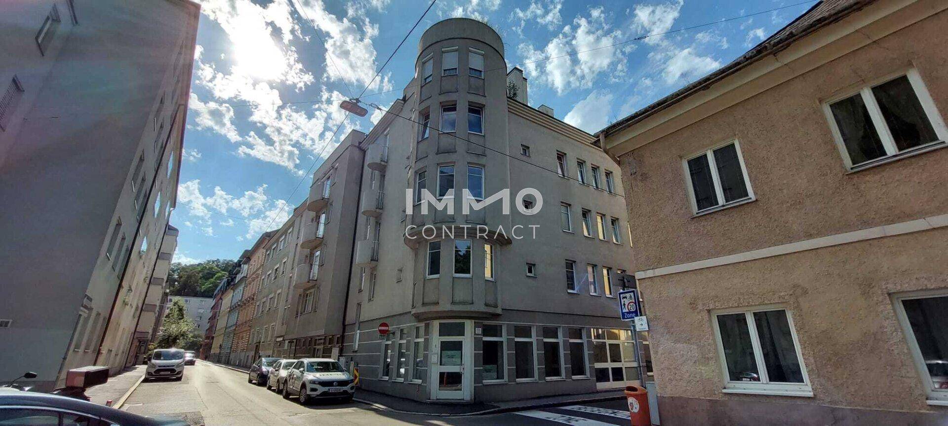 Mehrstöckiges Gebäude an einer Straßenecke in städtischer Umgebung unter blauem Himmel.