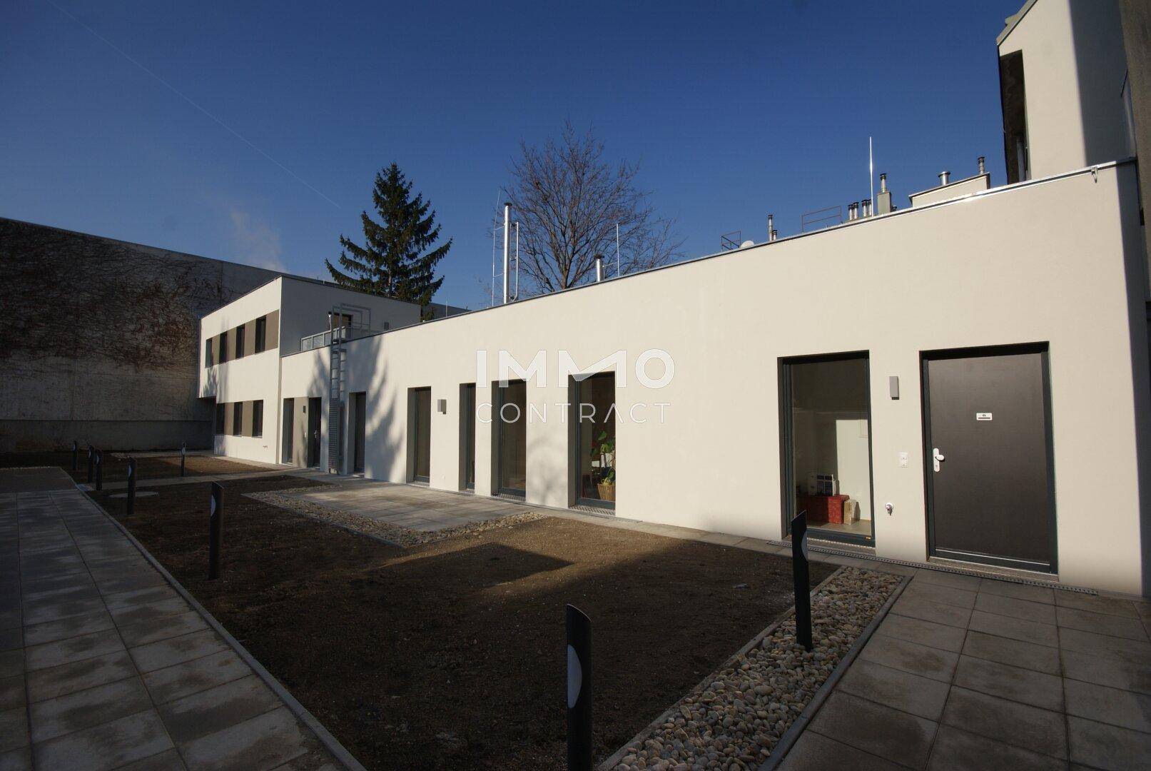Moderner Gebäudekomplex mit großen Glasfronten und einem neu angelegten Außenbereich mit Wegen.